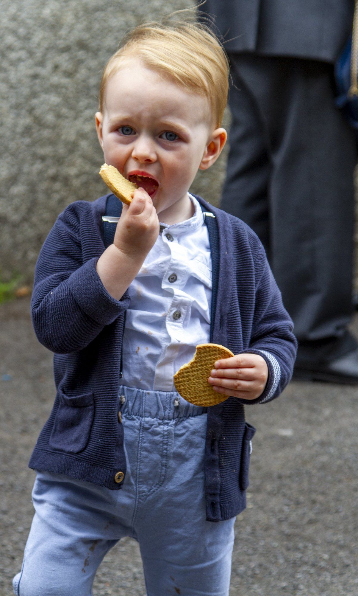 A little boy is eating a cookie on the street.