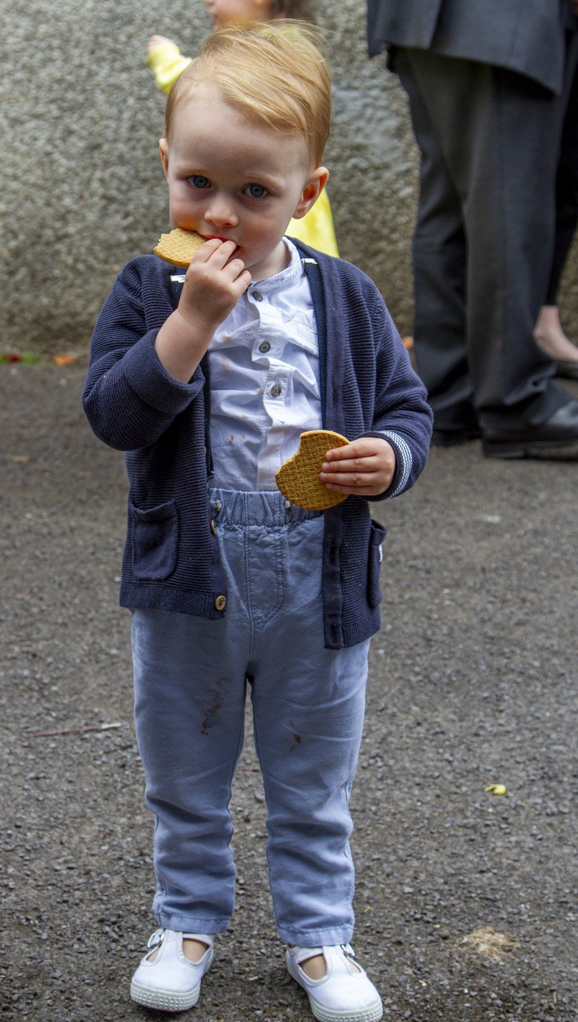 A little boy is standing on the sidewalk eating a cookie.