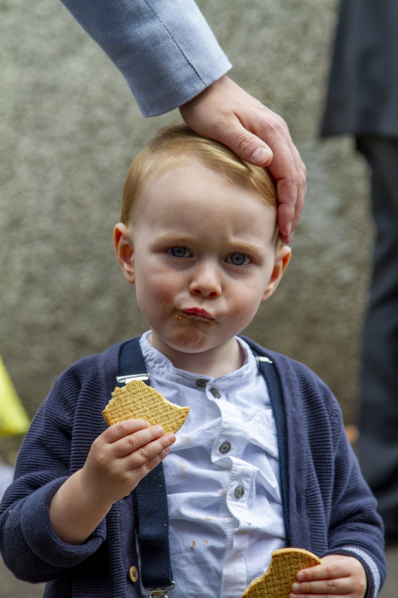 A little boy is eating a waffle and a person is petting his head.