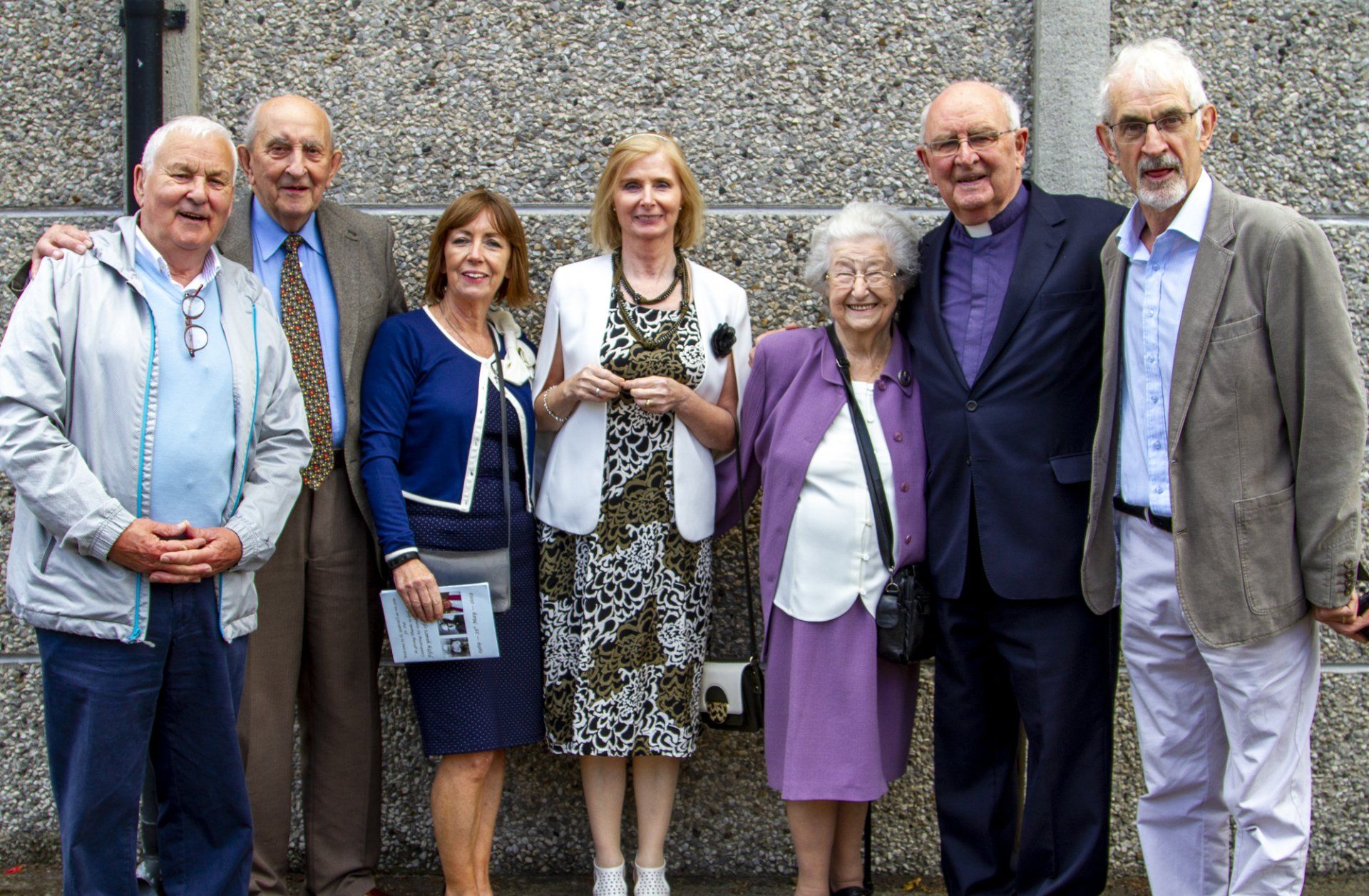 A group of people posing for a picture in front of a concrete wall