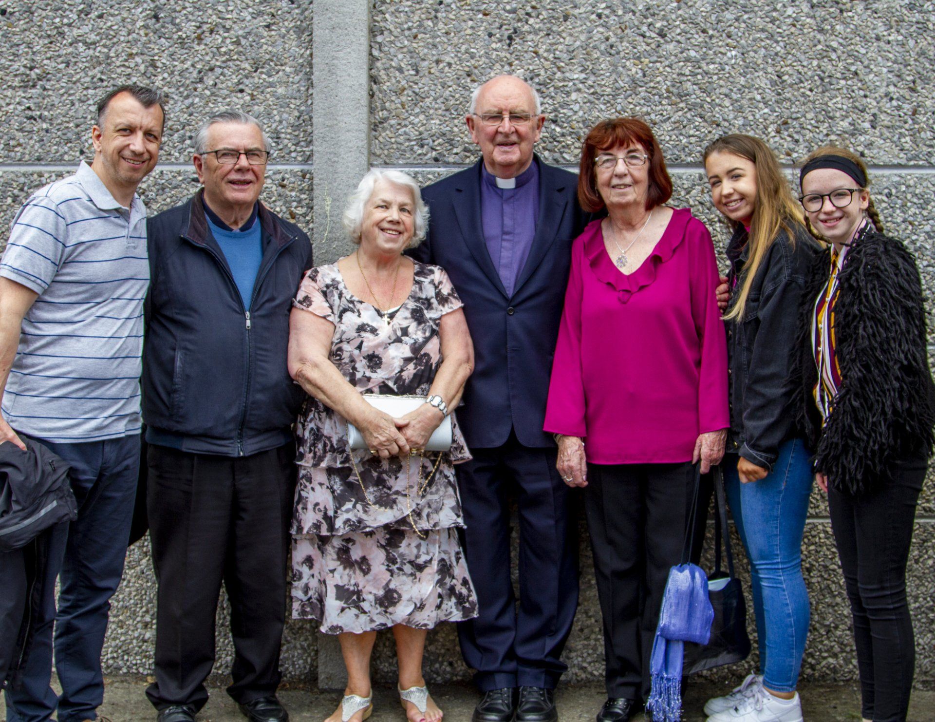 A group of people are posing for a picture in front of a concrete wall.