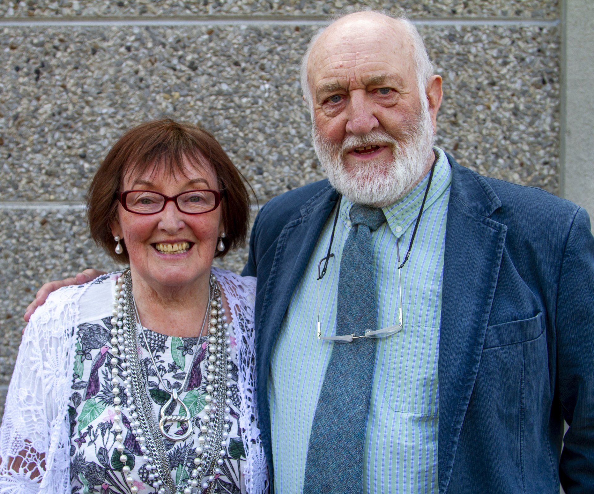 A man and a woman are posing for a picture in front of a concrete wall.