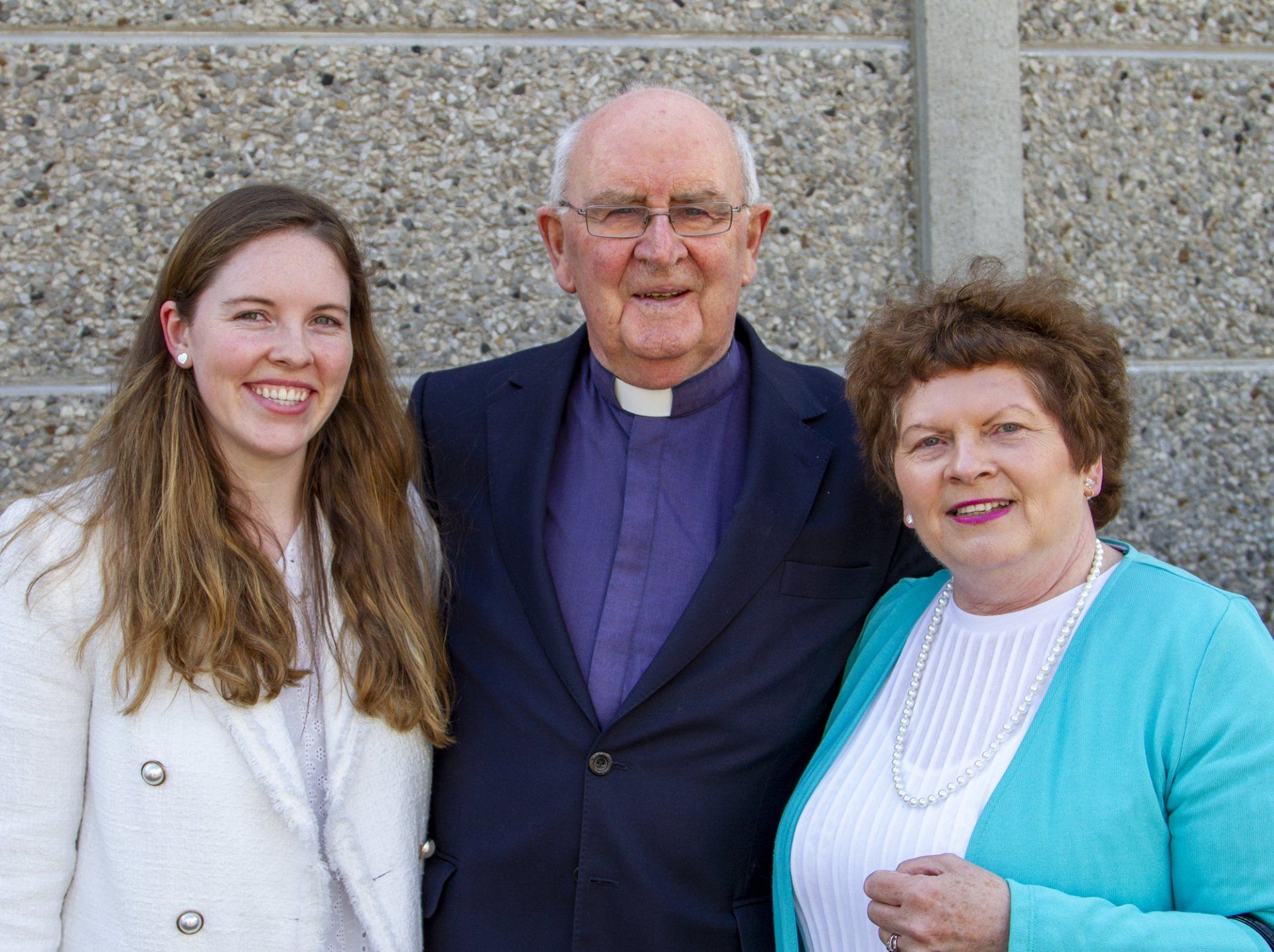 A man and two women are posing for a picture in front of a concrete wall.