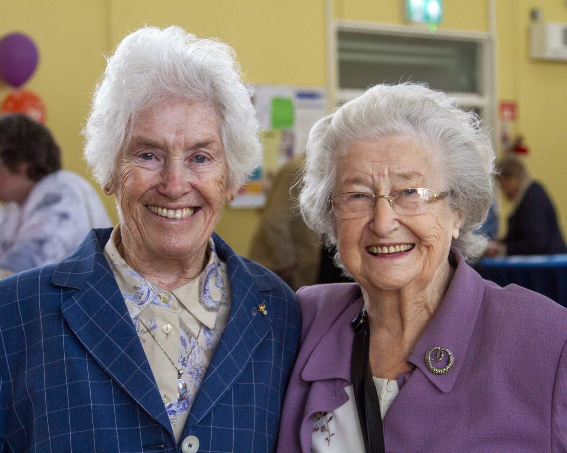 Two elderly women are posing for a picture together and smiling.