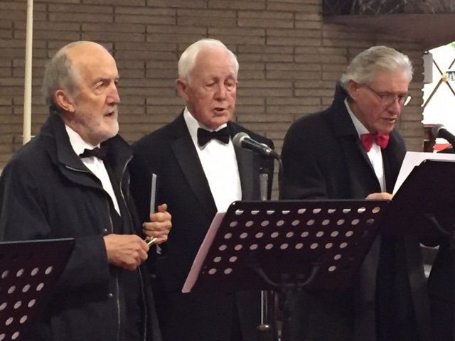 Three men in tuxedos are singing into microphones