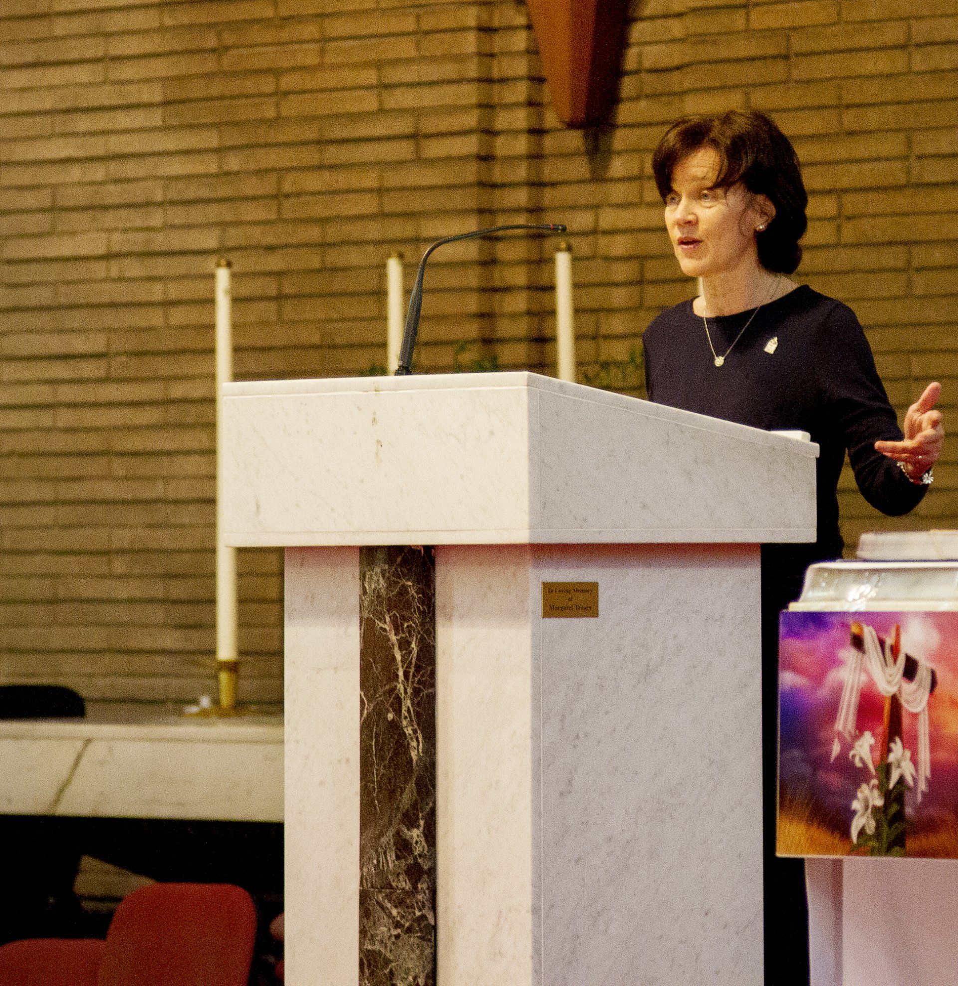 A woman stands at a podium in front of a brick wall