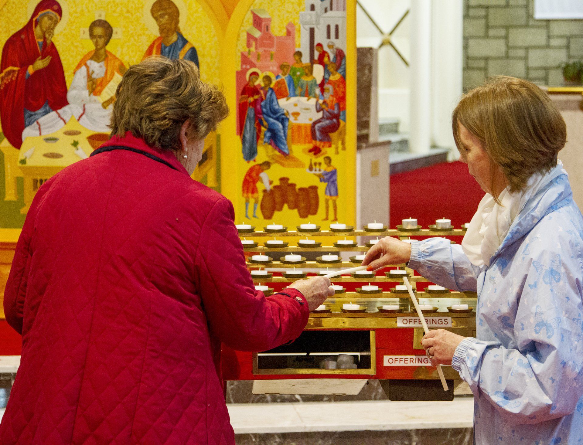 Two women are lighting candles in front of an icon in a church
