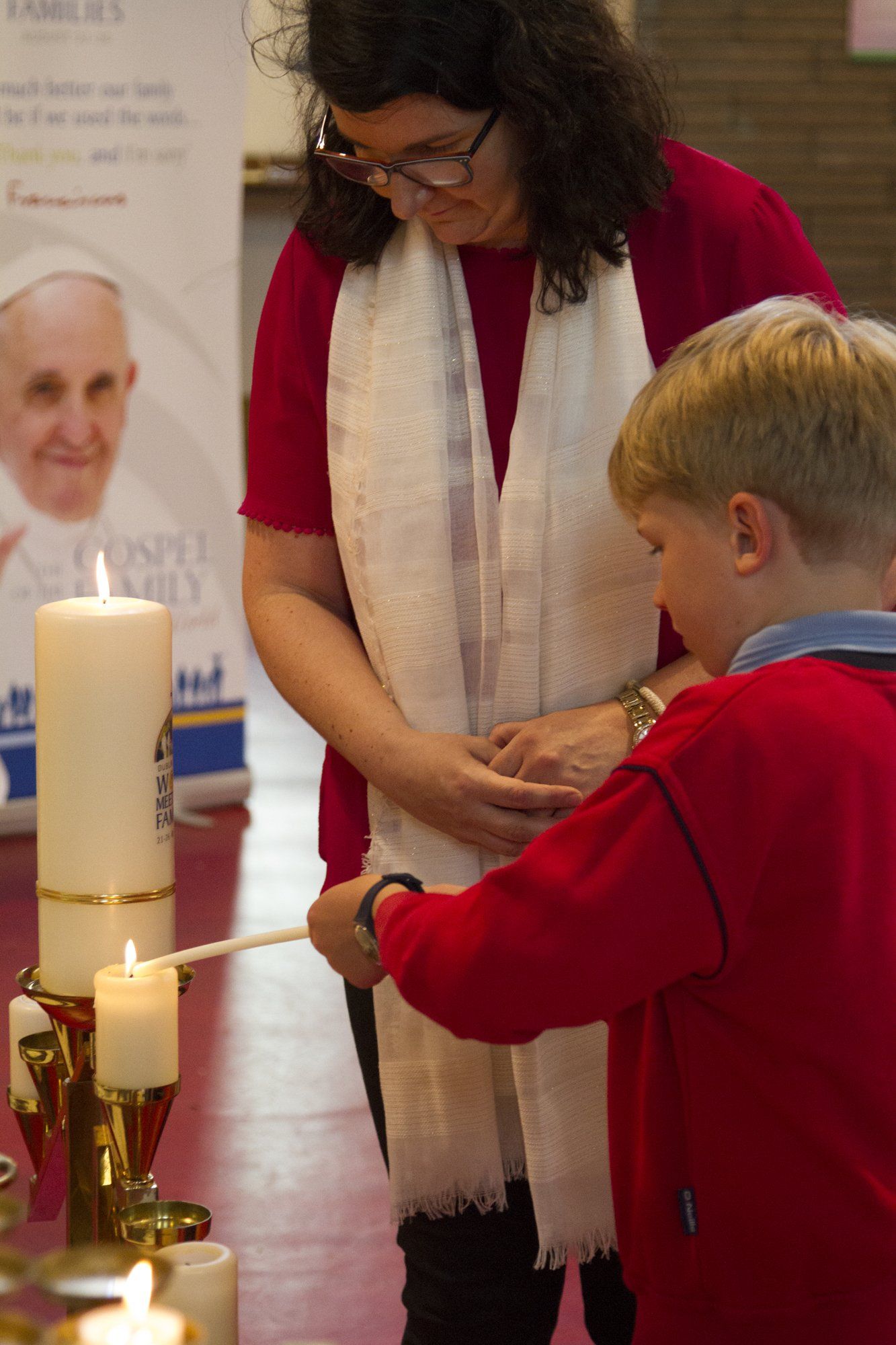 A woman and a boy are lighting candles in a church.