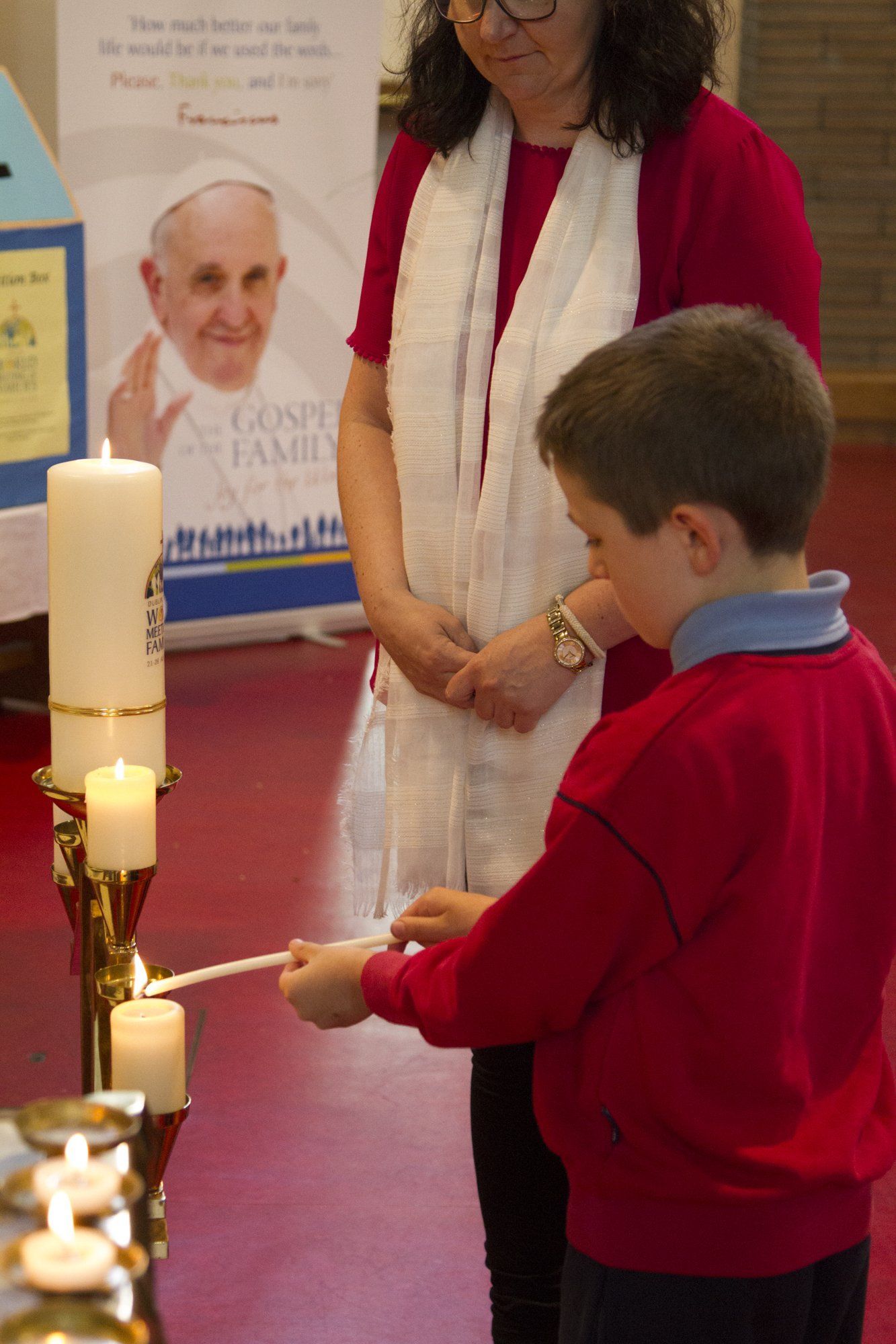 A boy in a red shirt is lighting a candle