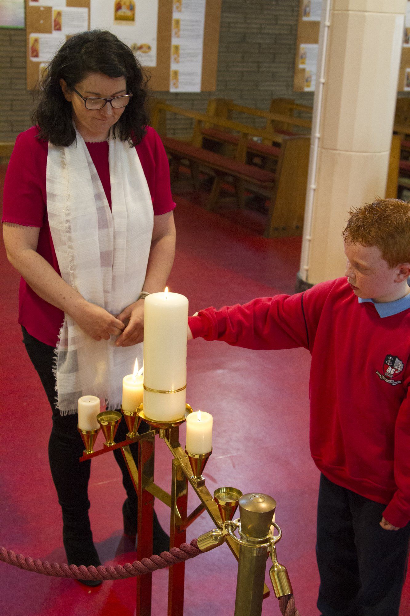 A woman and a boy are lighting candles in a church