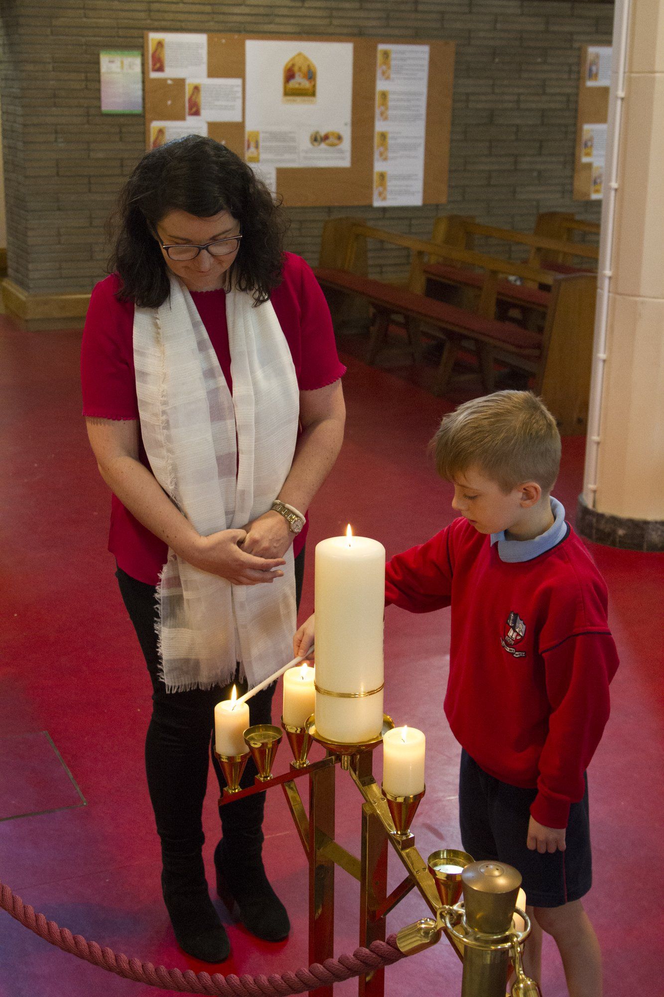 A woman and a boy are lighting candles in a church.