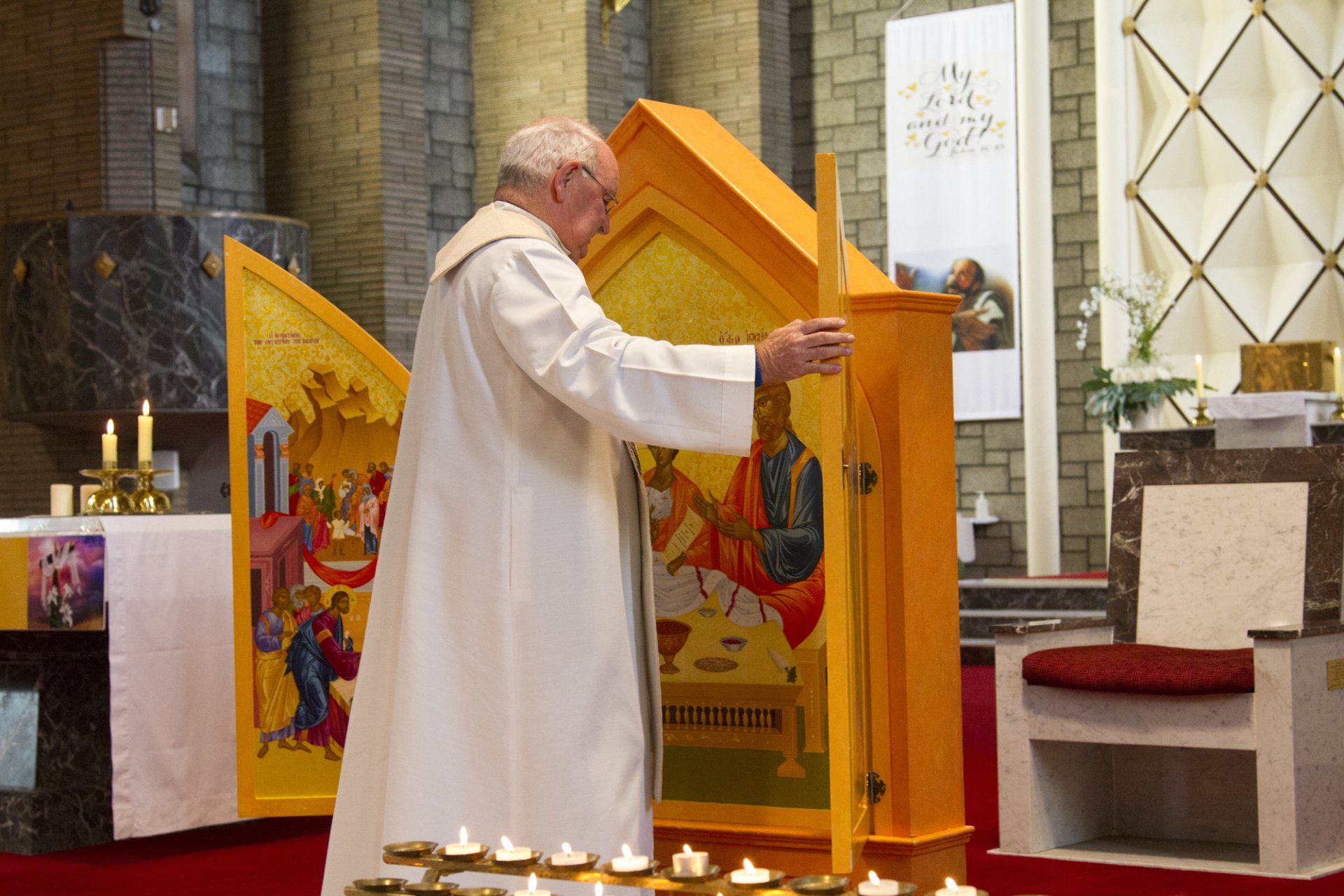 A man in a white robe is standing in front of an altar with candles.