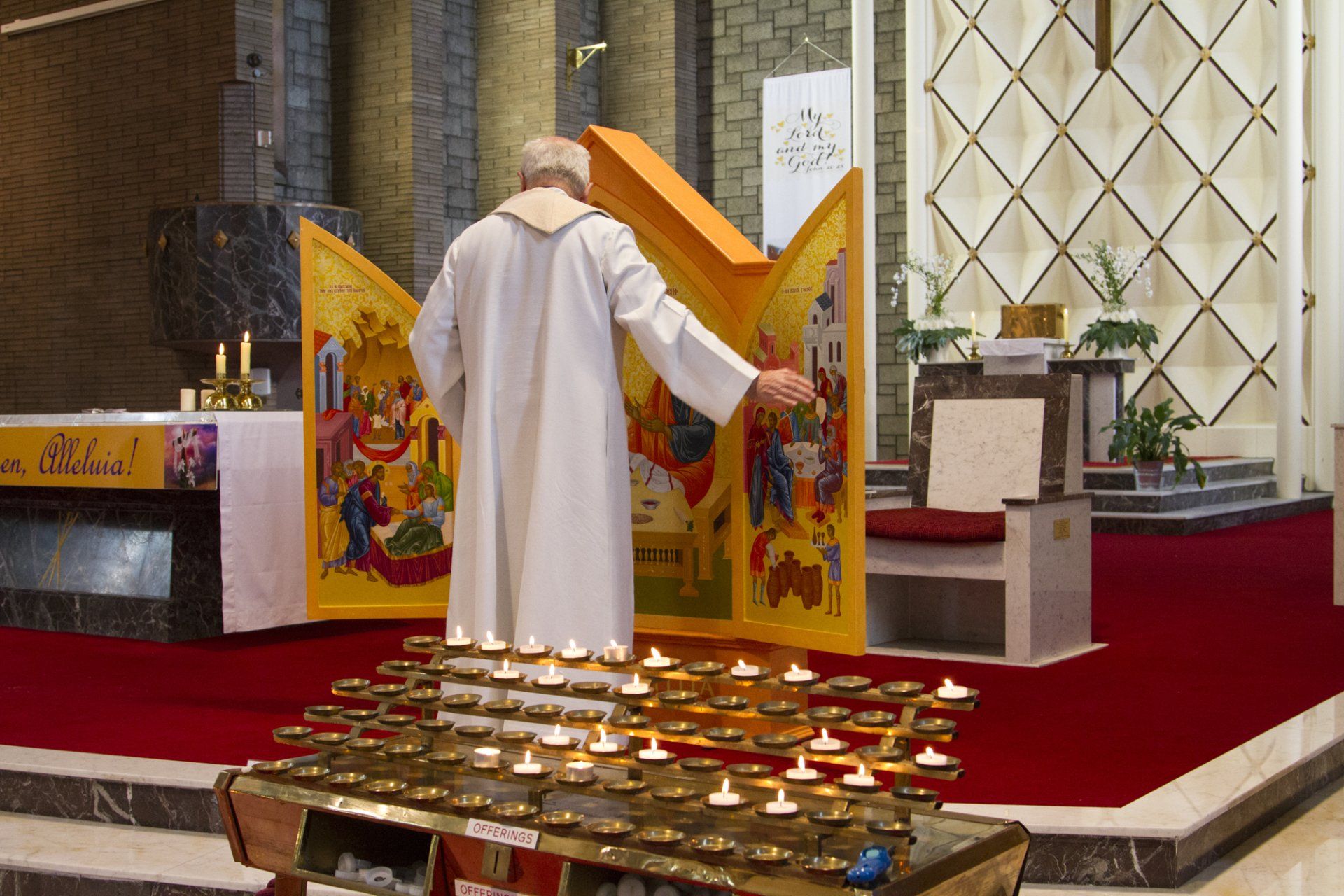A man in a white robe is standing in front of a candle holder in a church