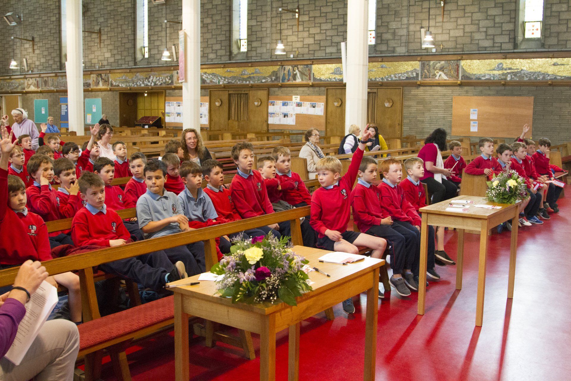 A group of children are sitting in a church raising their hands