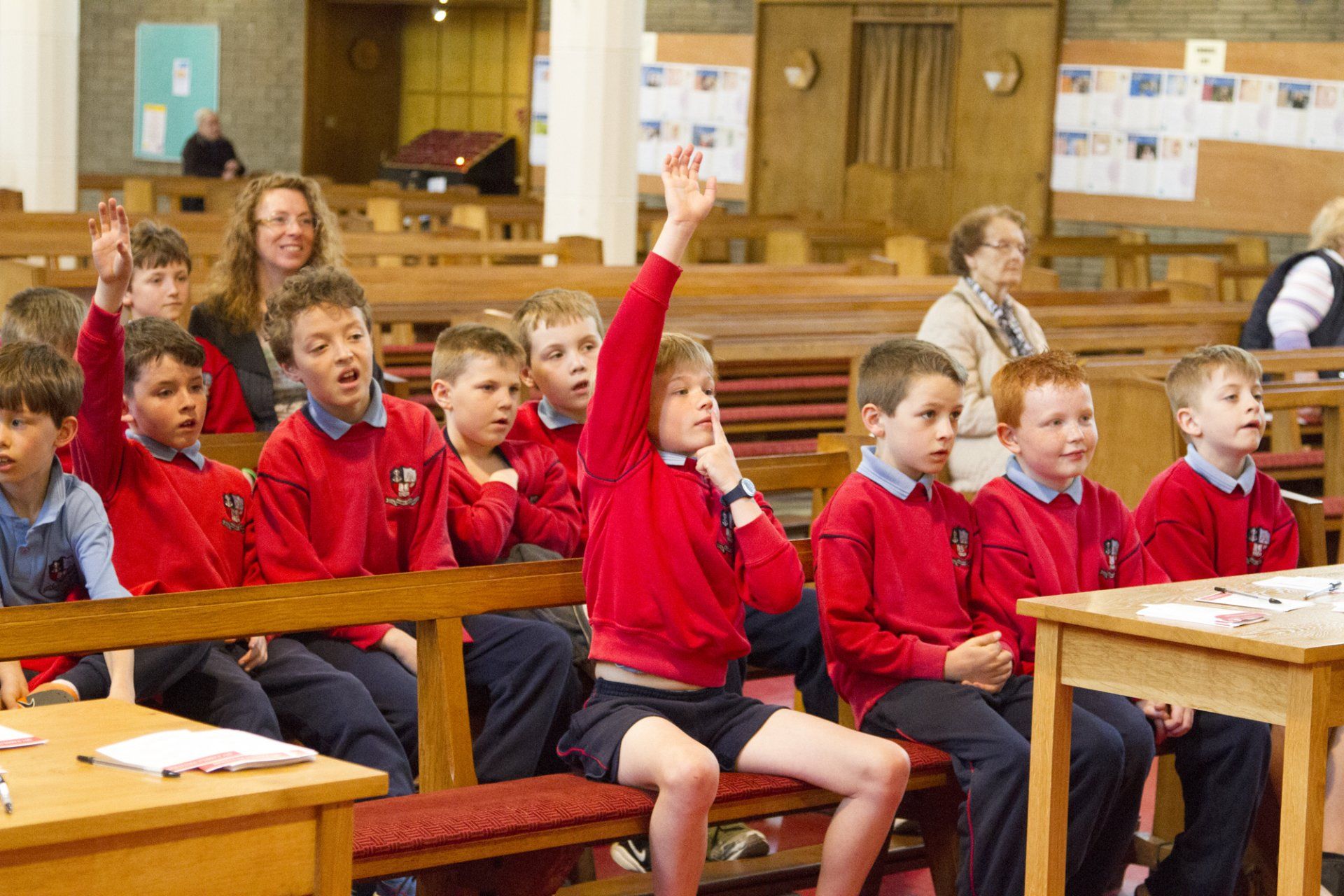 A group of children are sitting in a church raising their hands to answer a question.