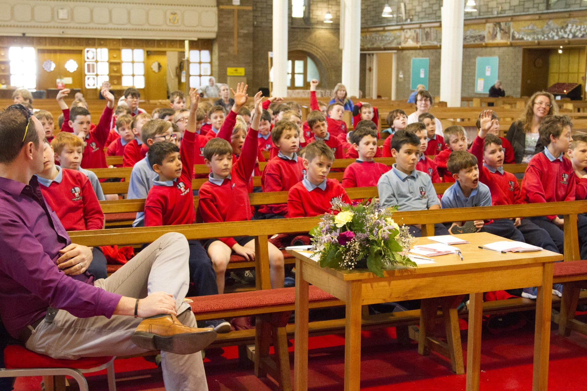 A group of children in red shirts are raising their hands in a church