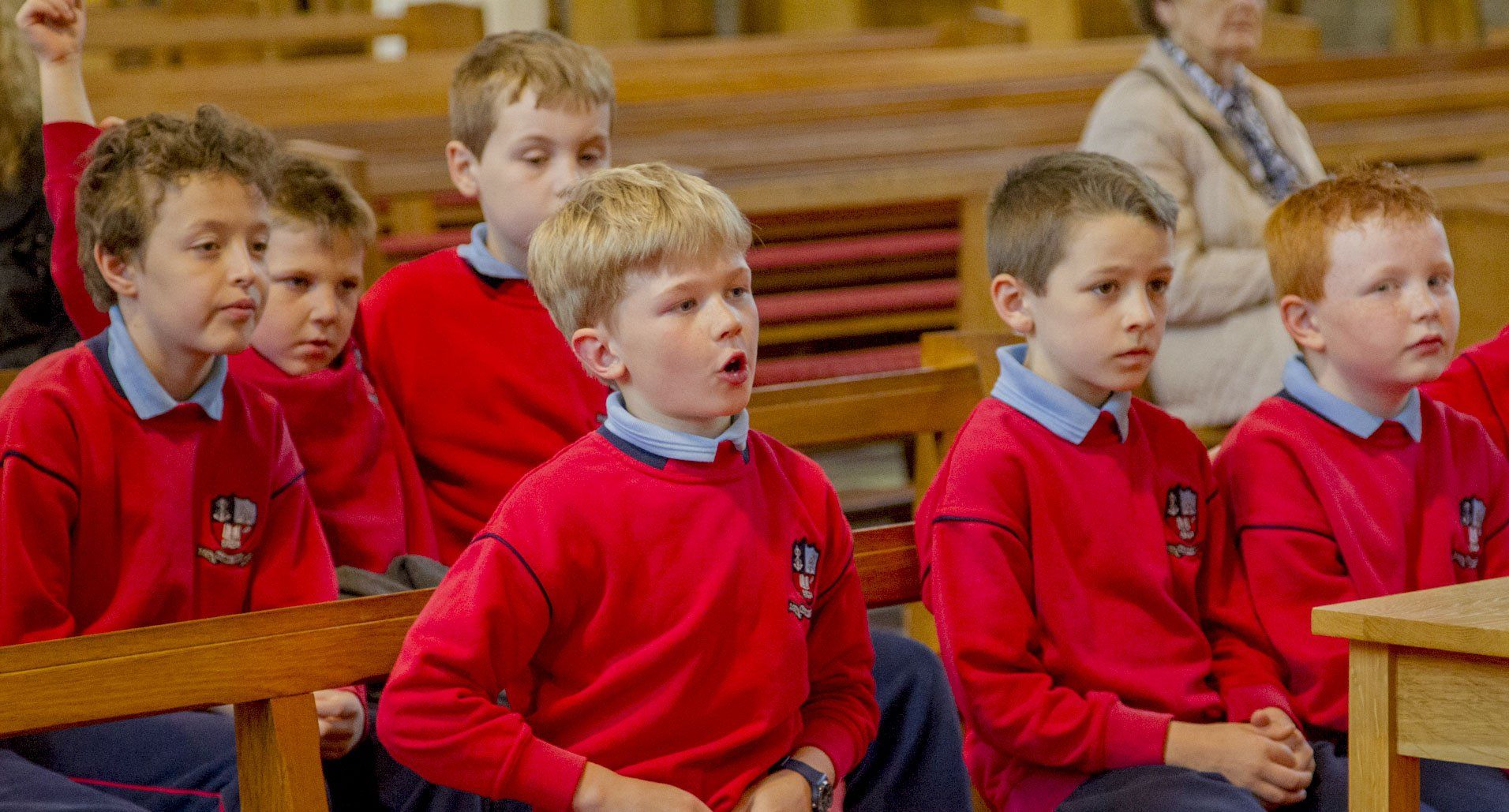 A group of young boys in red uniforms are sitting in a church.