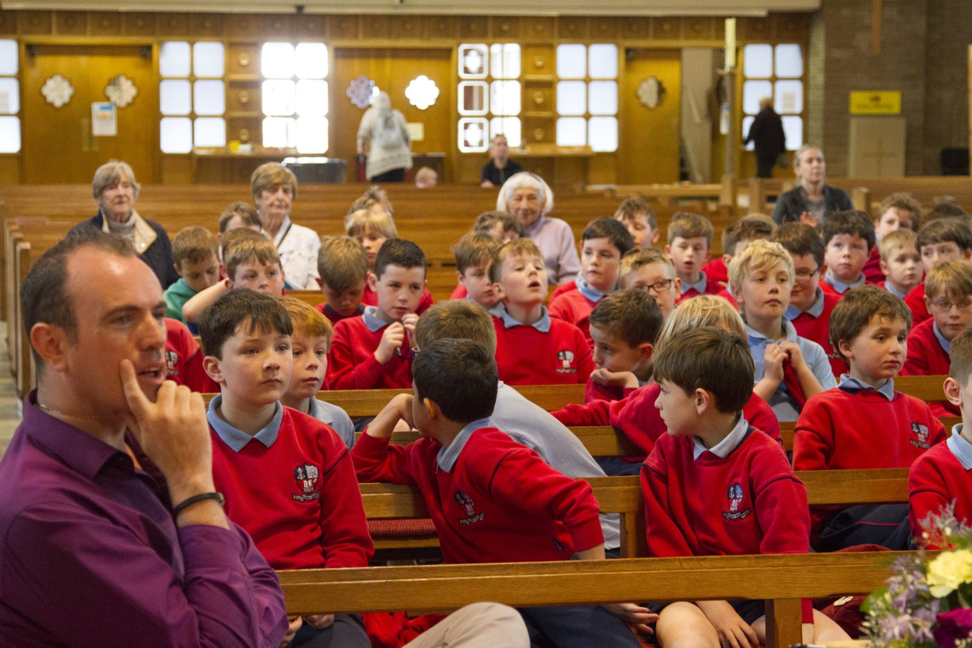 A group of children in red sweaters are sitting in a church.