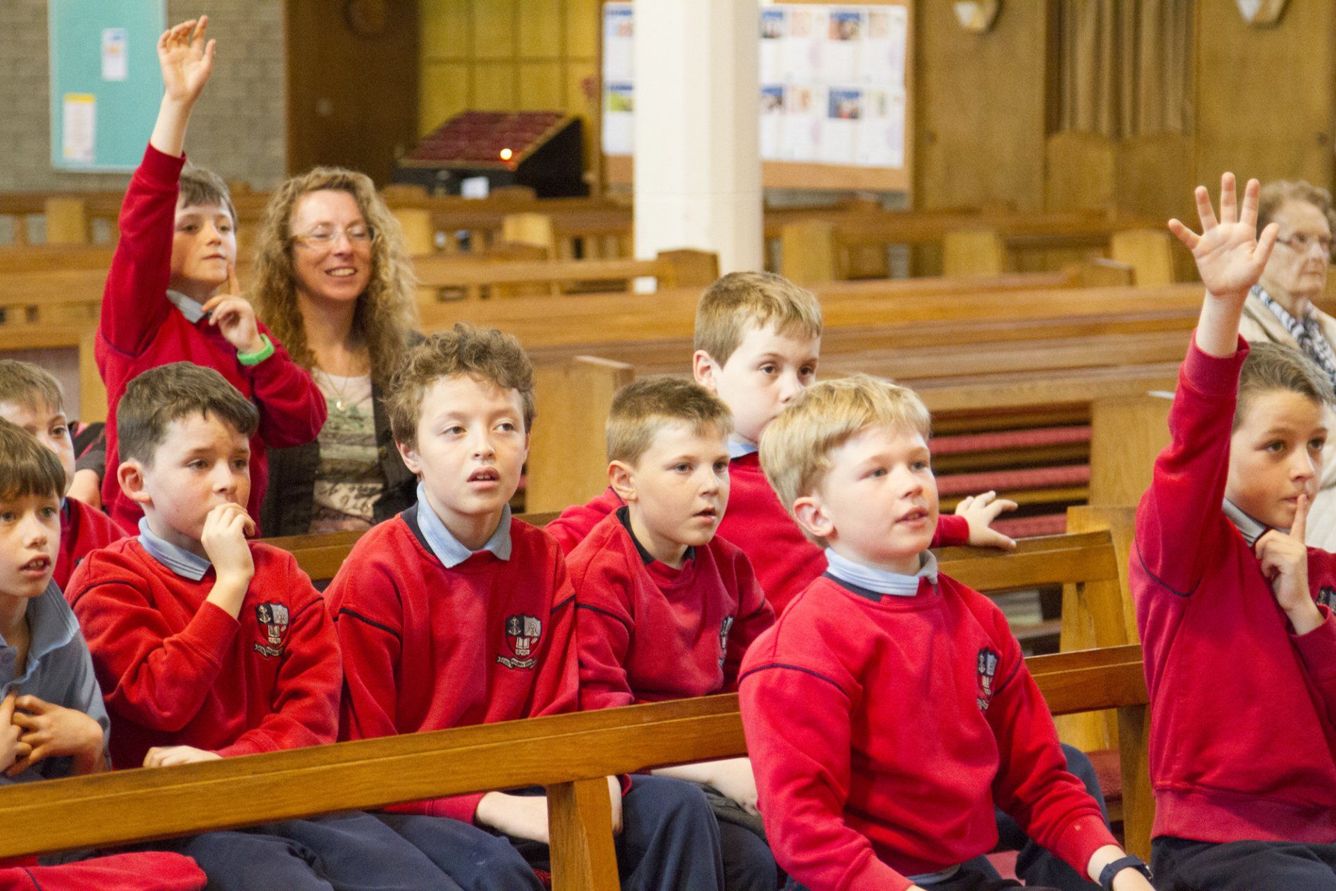 A group of children in red shirts are raising their hands in a church.