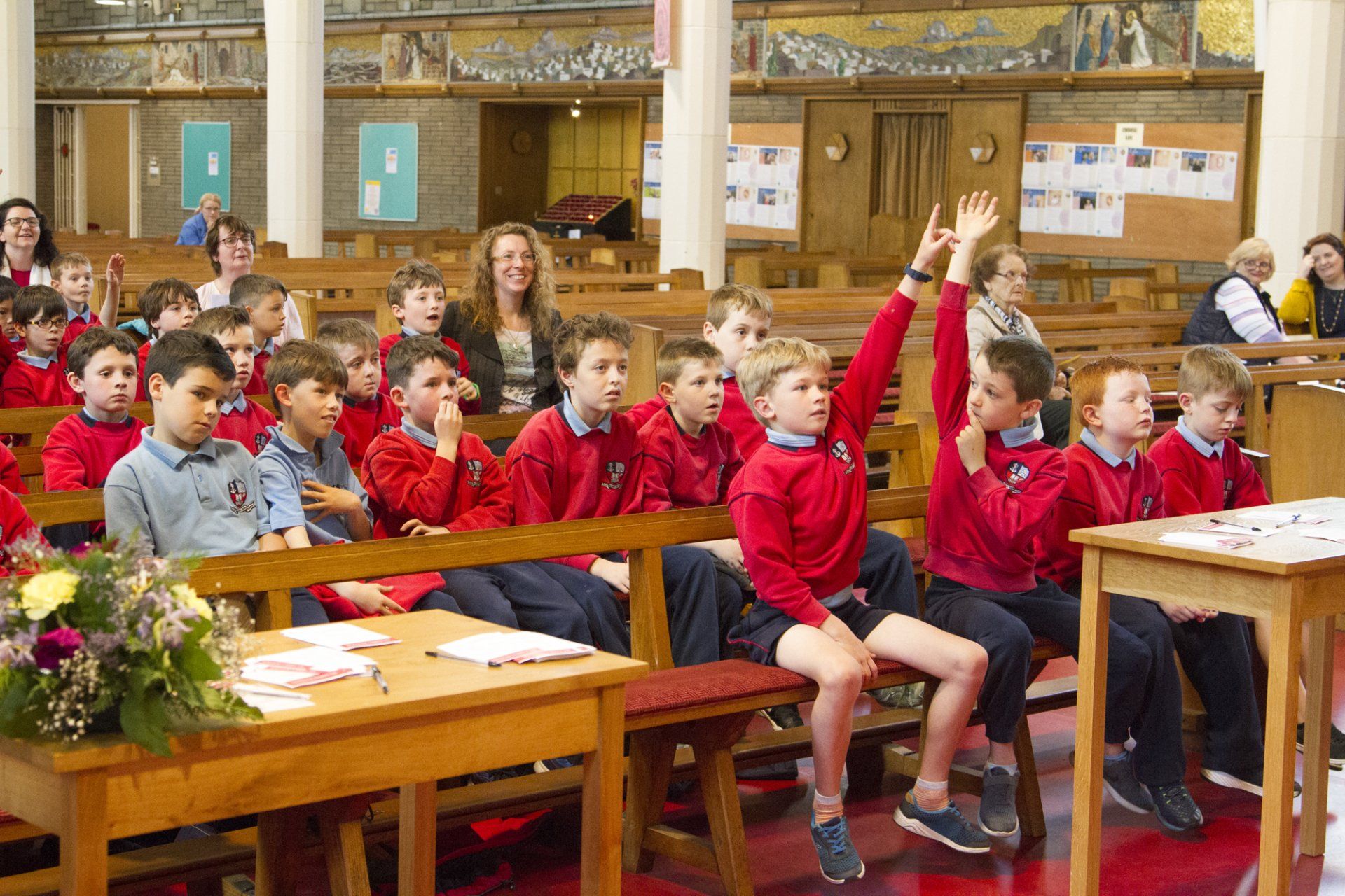 A group of children are sitting in a church with their hands up.