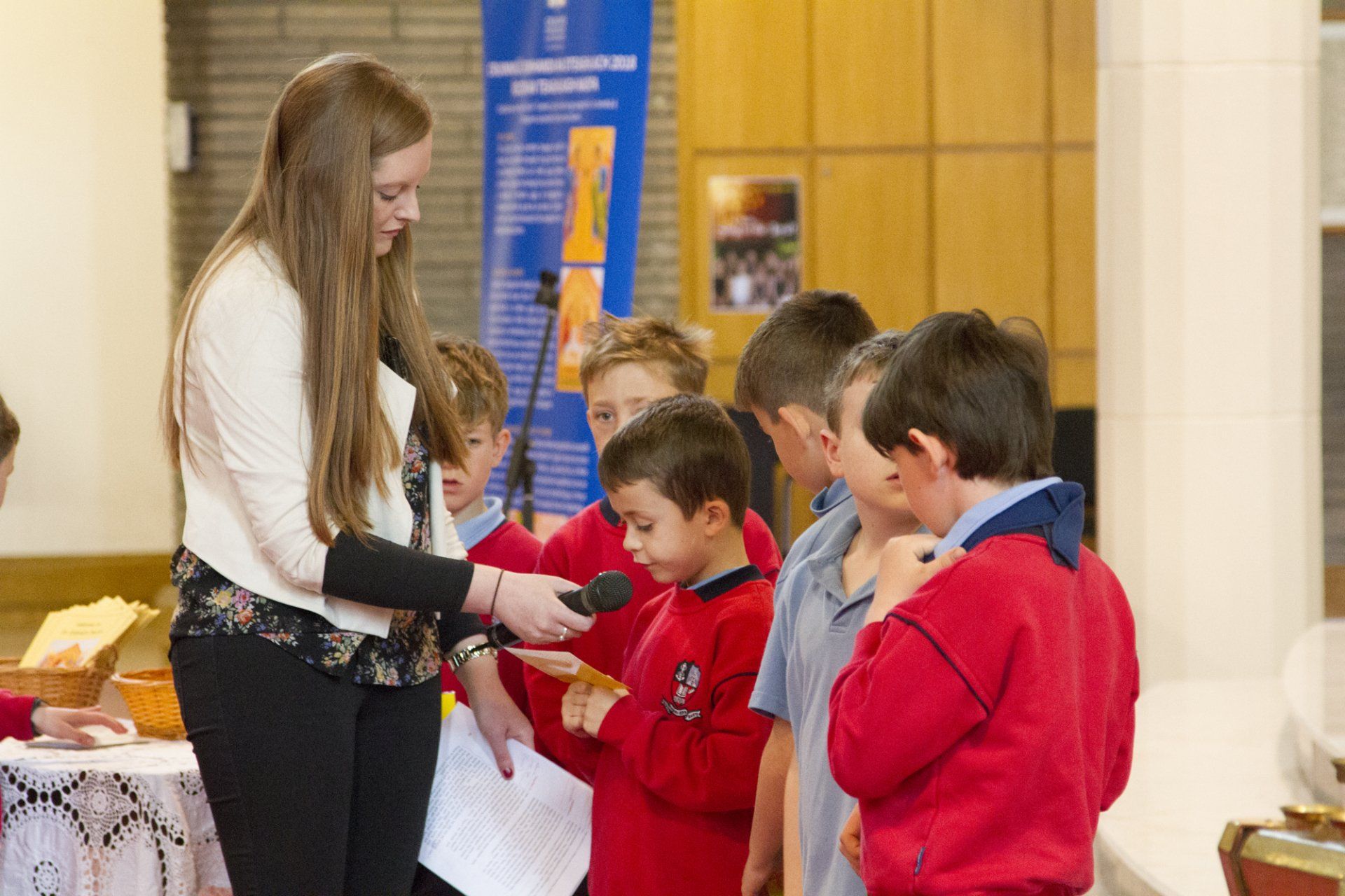 A woman is holding a microphone in front of a group of children.