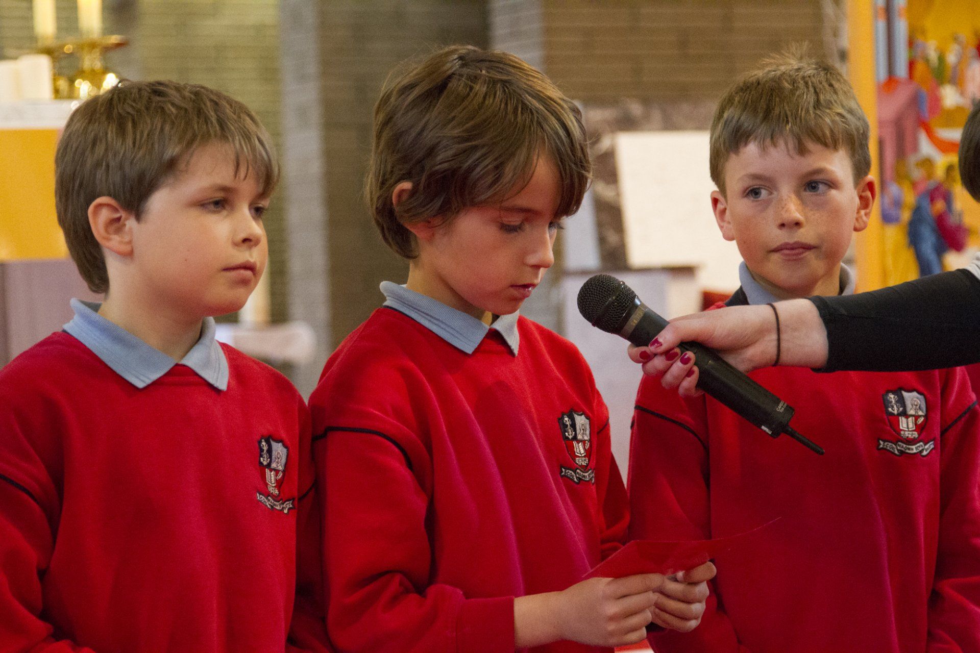 Three young boys in red sweaters are being interviewed by a person holding a microphone.