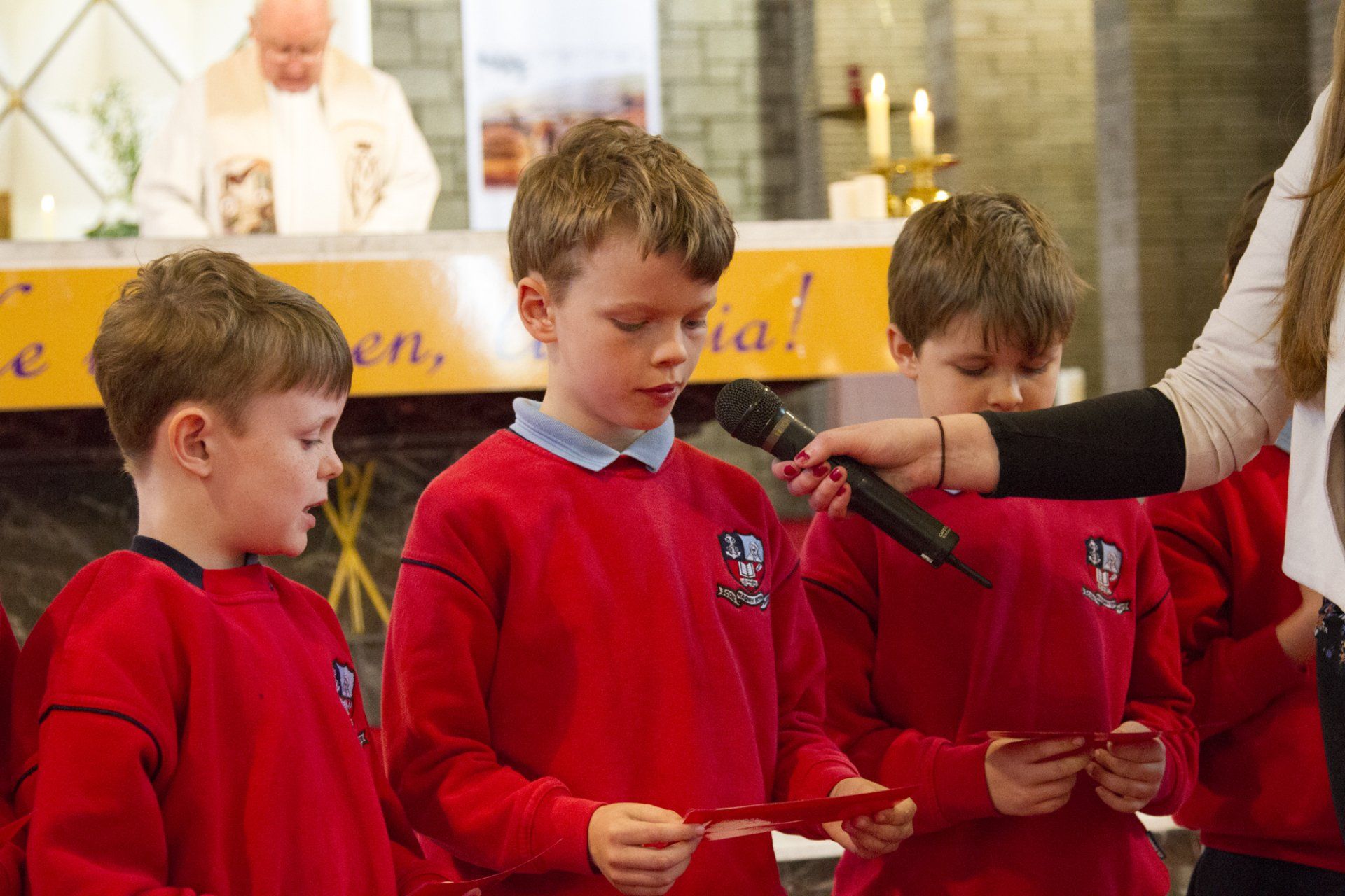 A group of young boys in red sweaters are singing into microphones in a church.
