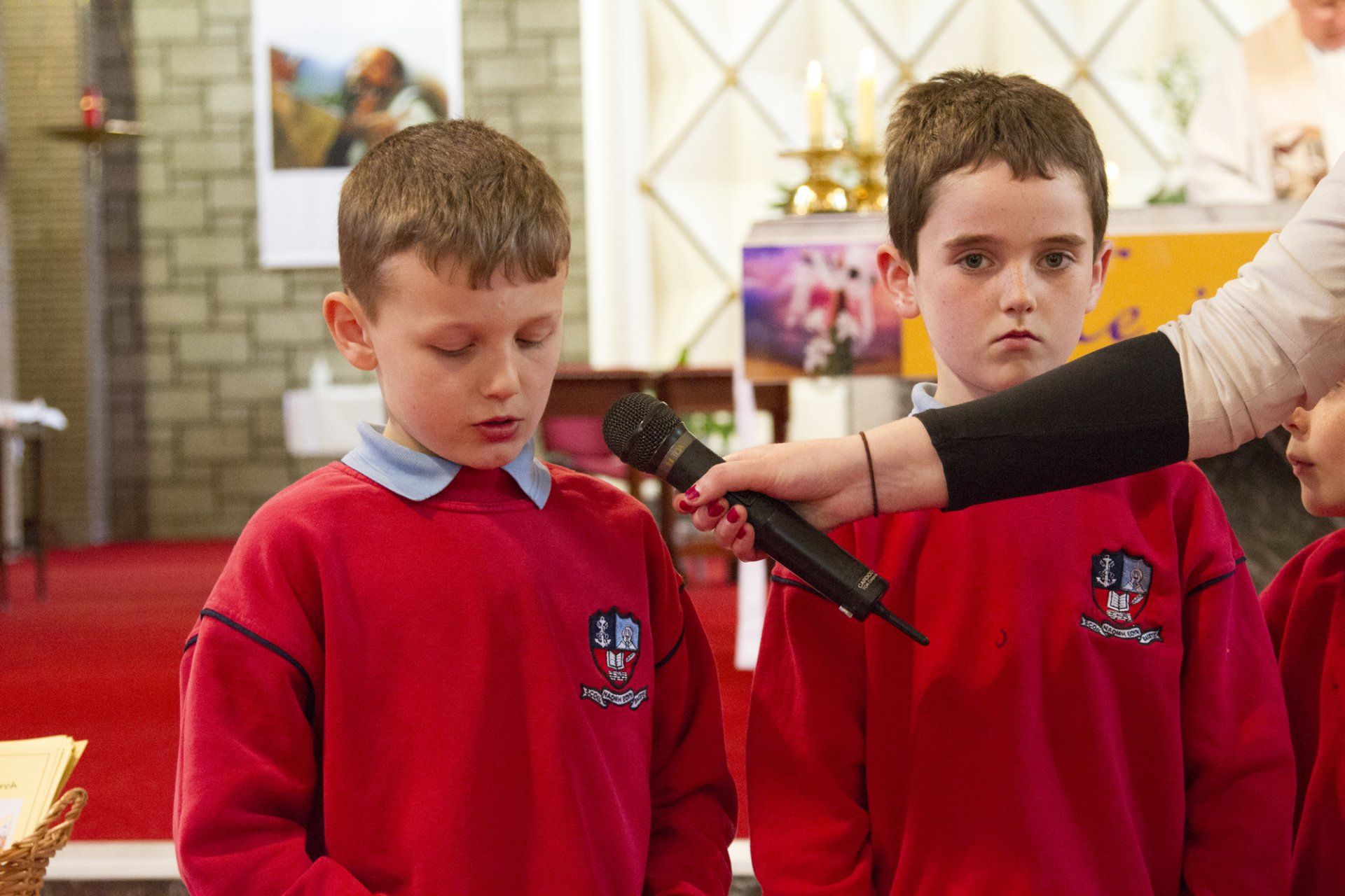 A woman is holding a microphone over two young boys in red sweaters.