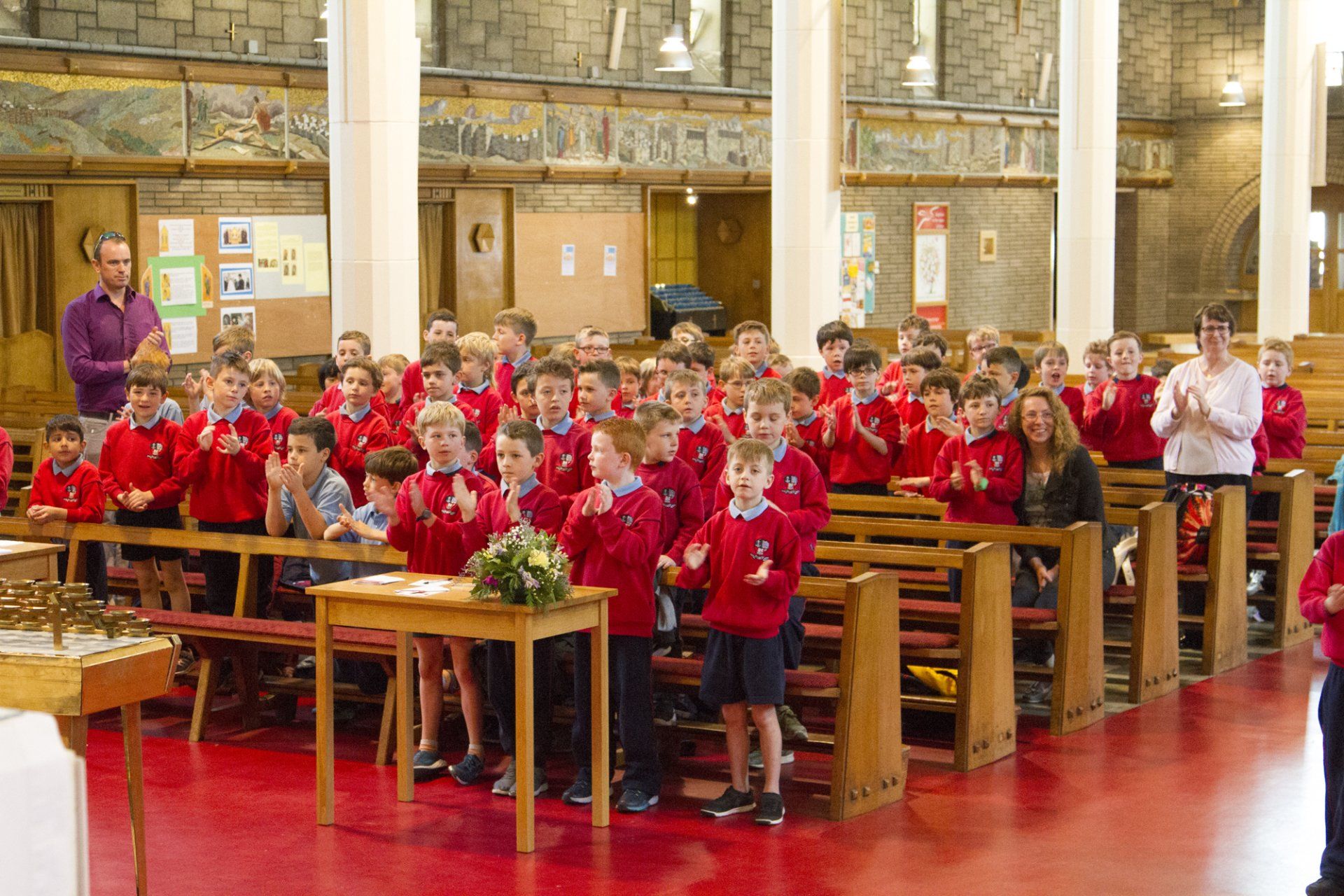 A large group of children in red jackets are clapping in a church.