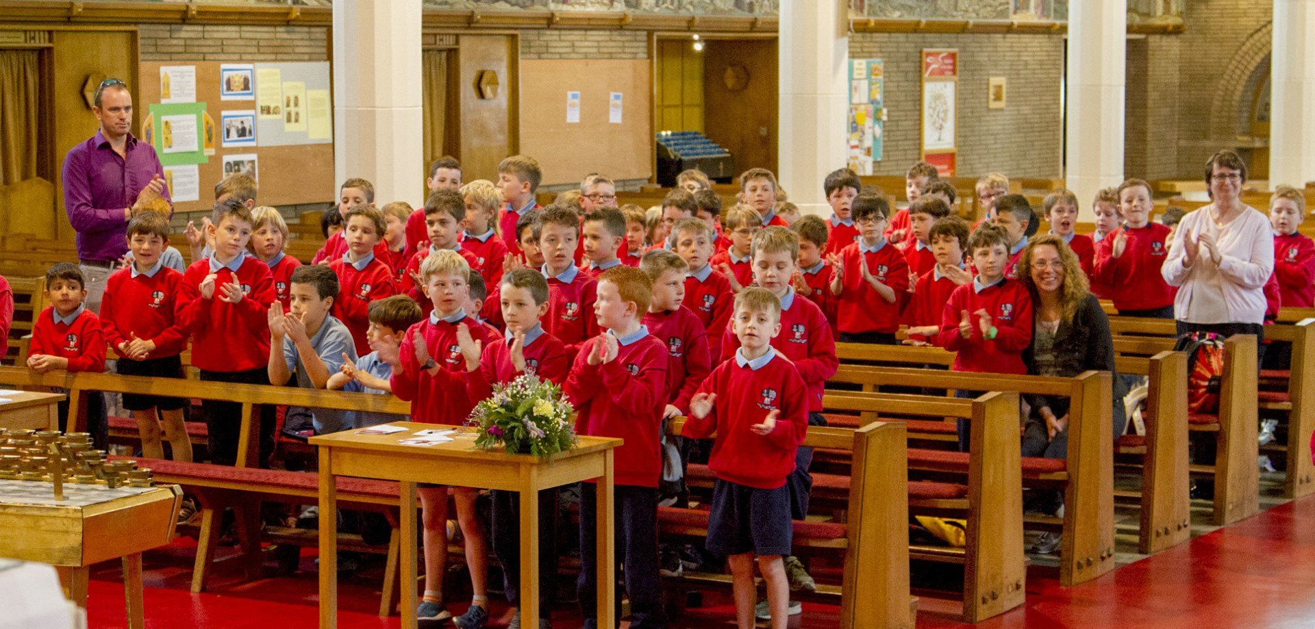 A large group of children in red shirts are sitting in a church.