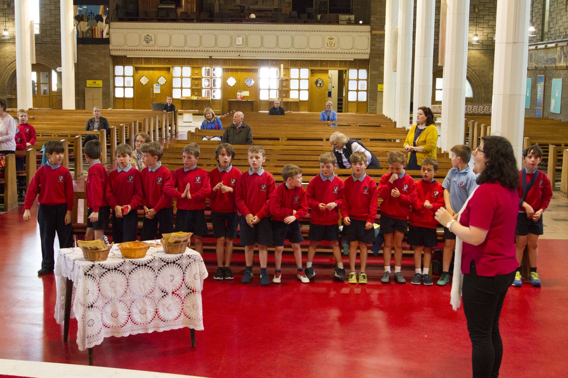 A woman in a red shirt stands in front of a group of children
