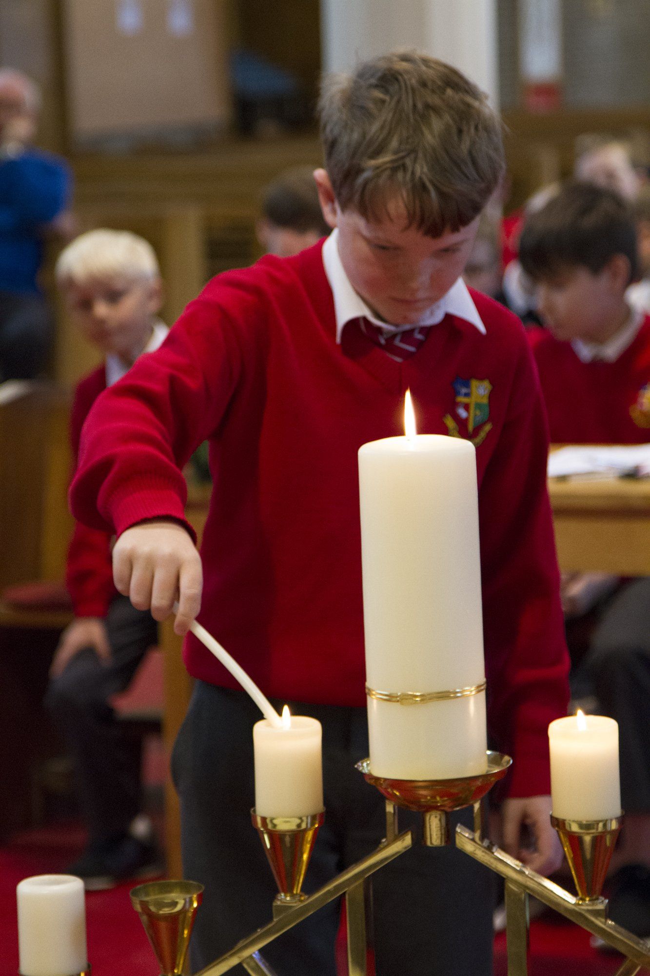 A boy in a red sweater is lighting a candle in a church.