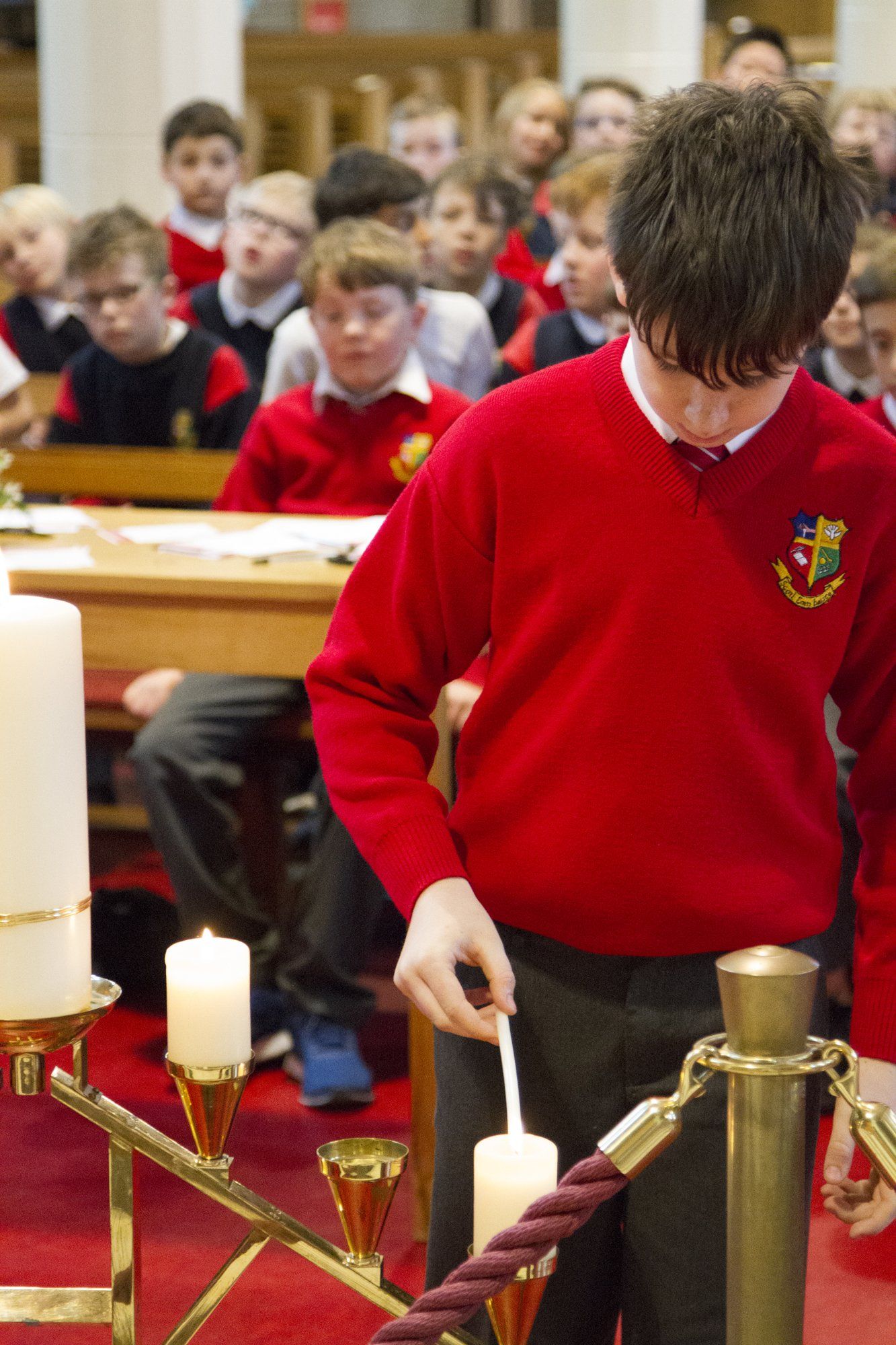 A boy in a red sweater is lighting a candle in a church