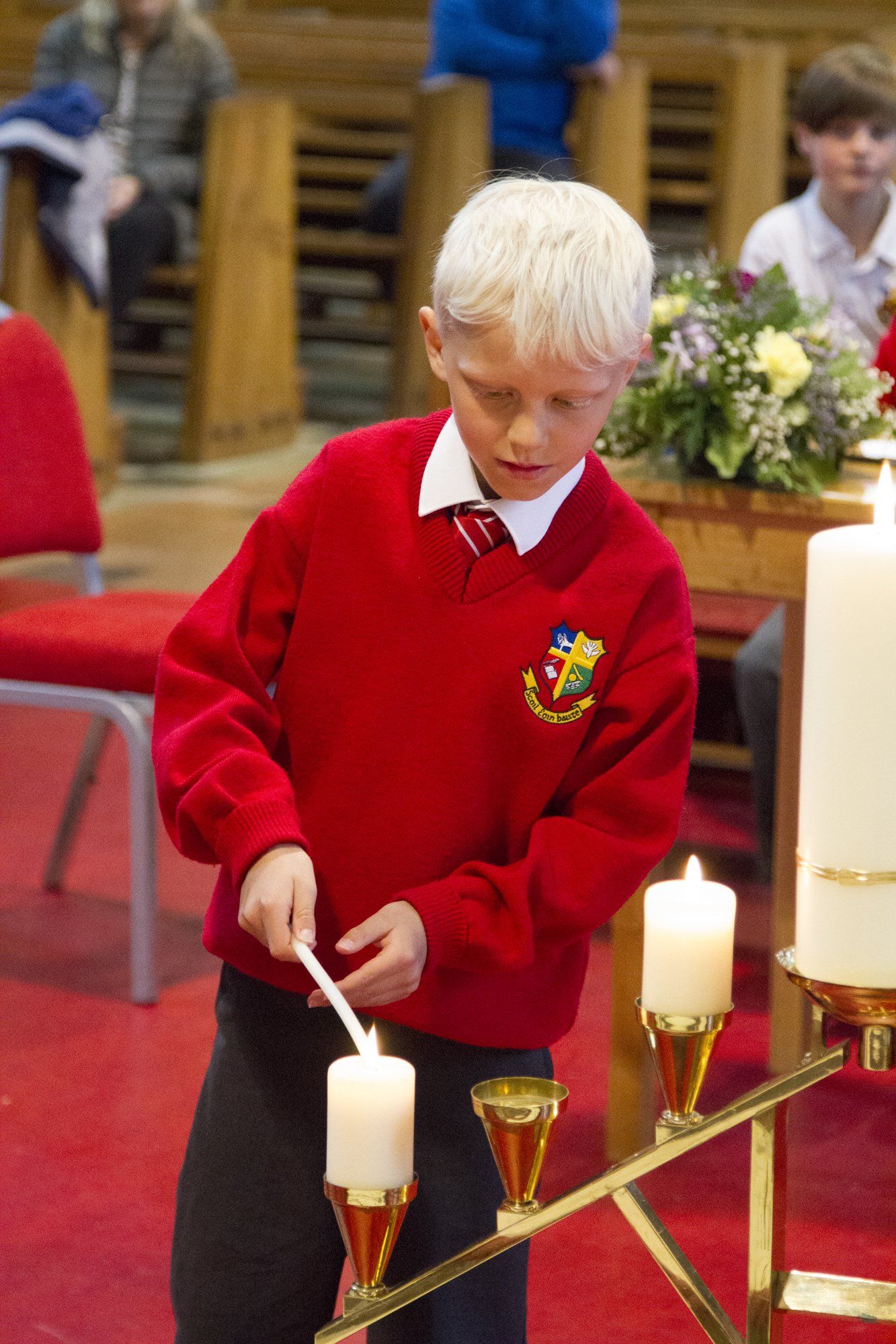 A young boy in a red sweater is lighting a candle