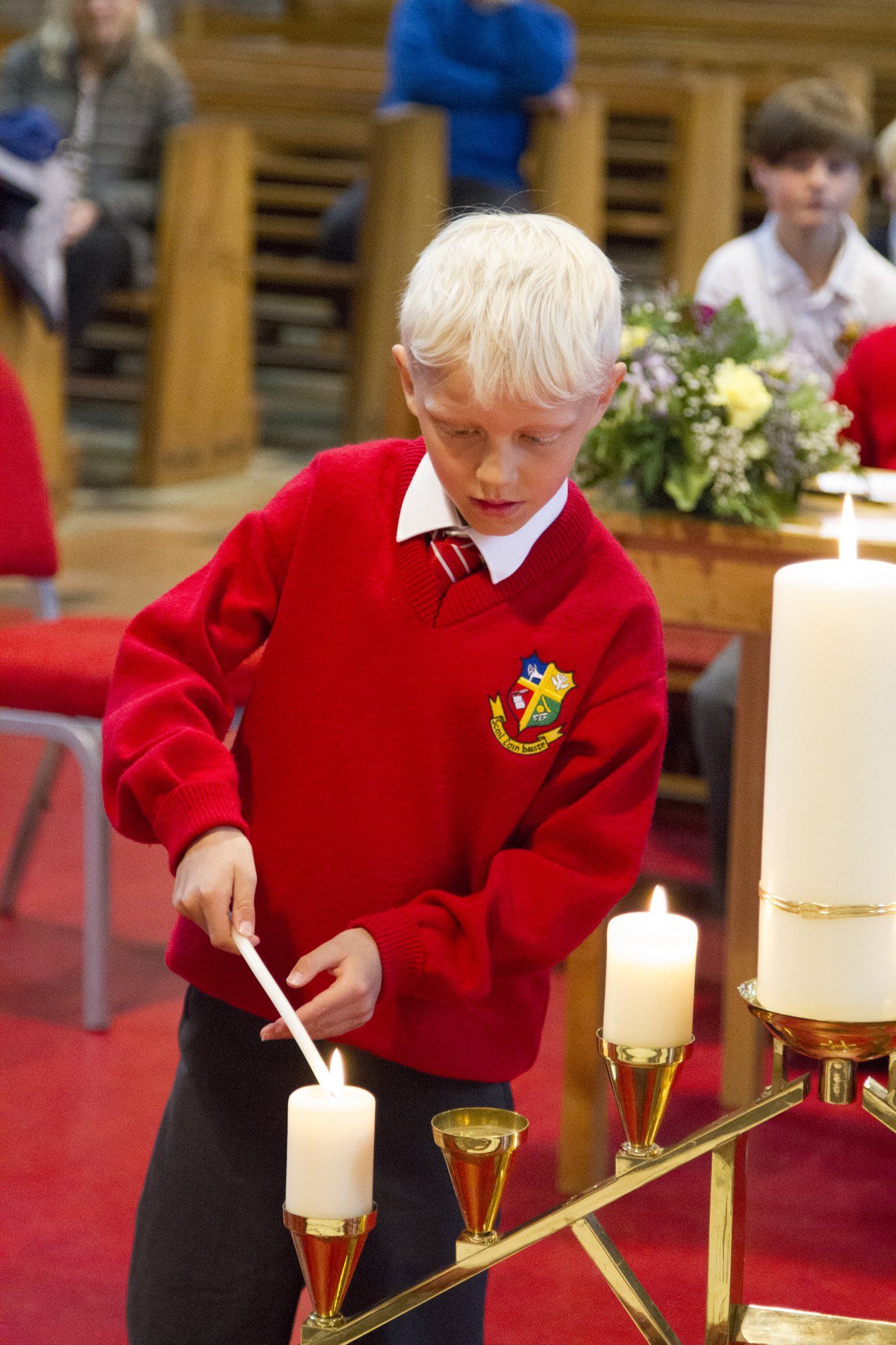 A young boy in a red sweater is lighting a candle