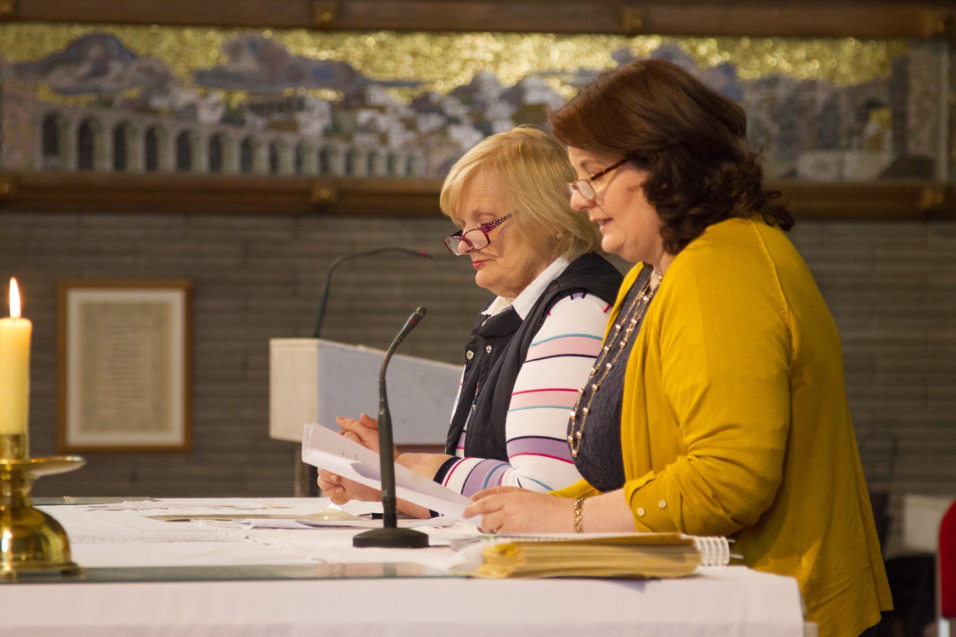 Two women are sitting at a table in front of microphones in a church.