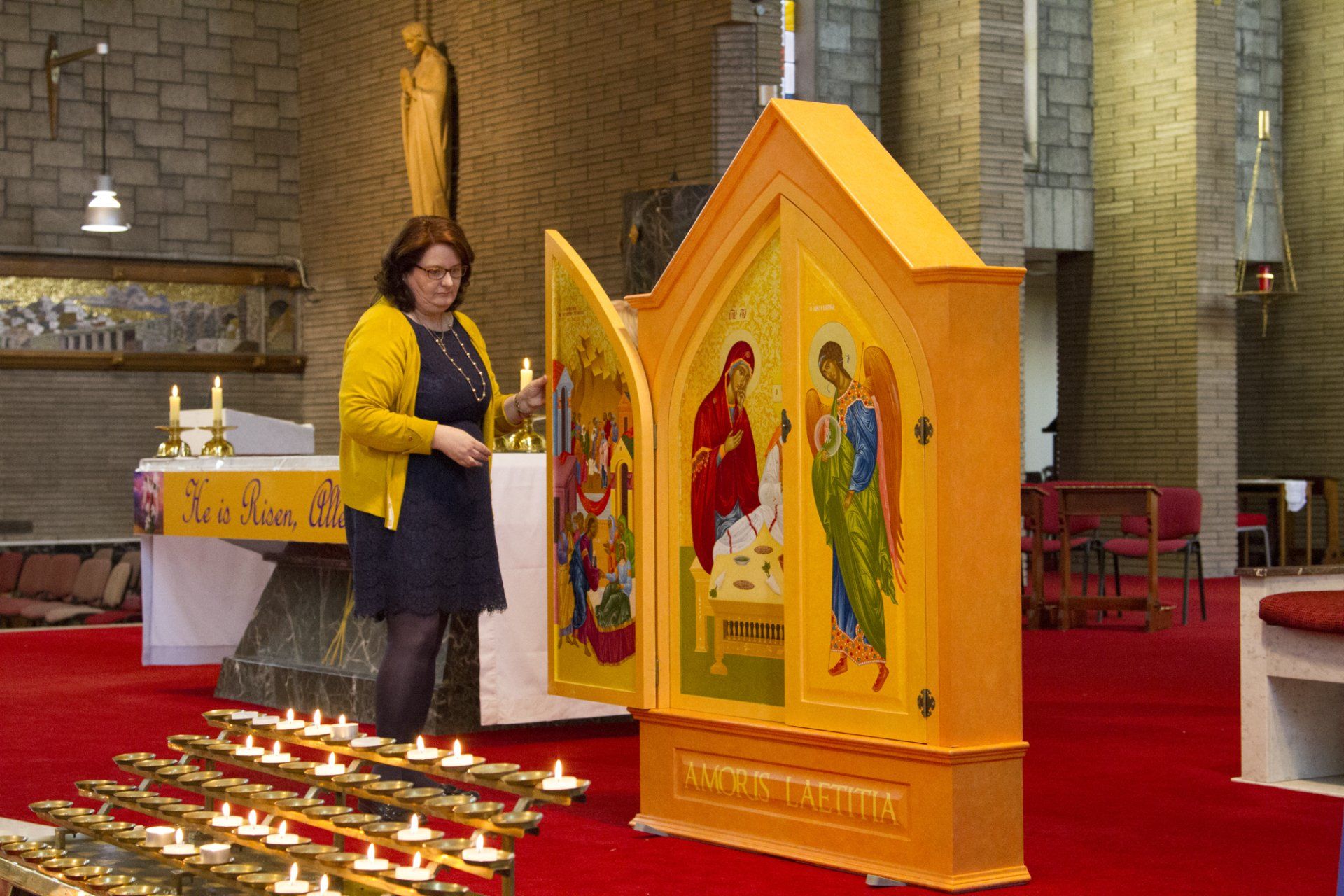 A woman in a yellow jacket is standing in front of a yellow altar in a church.