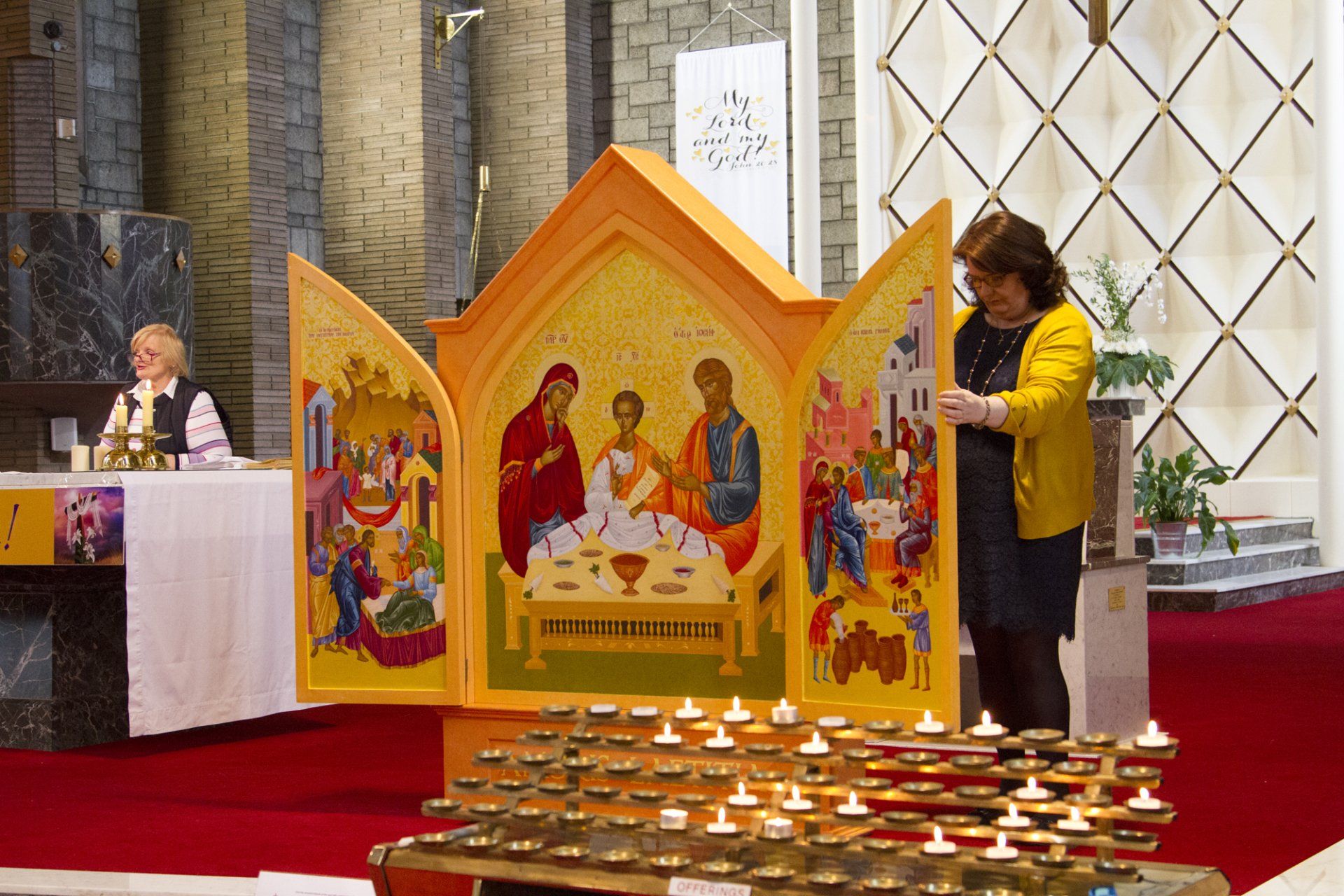 A woman in a yellow jacket is standing next to a candle holder in a church.