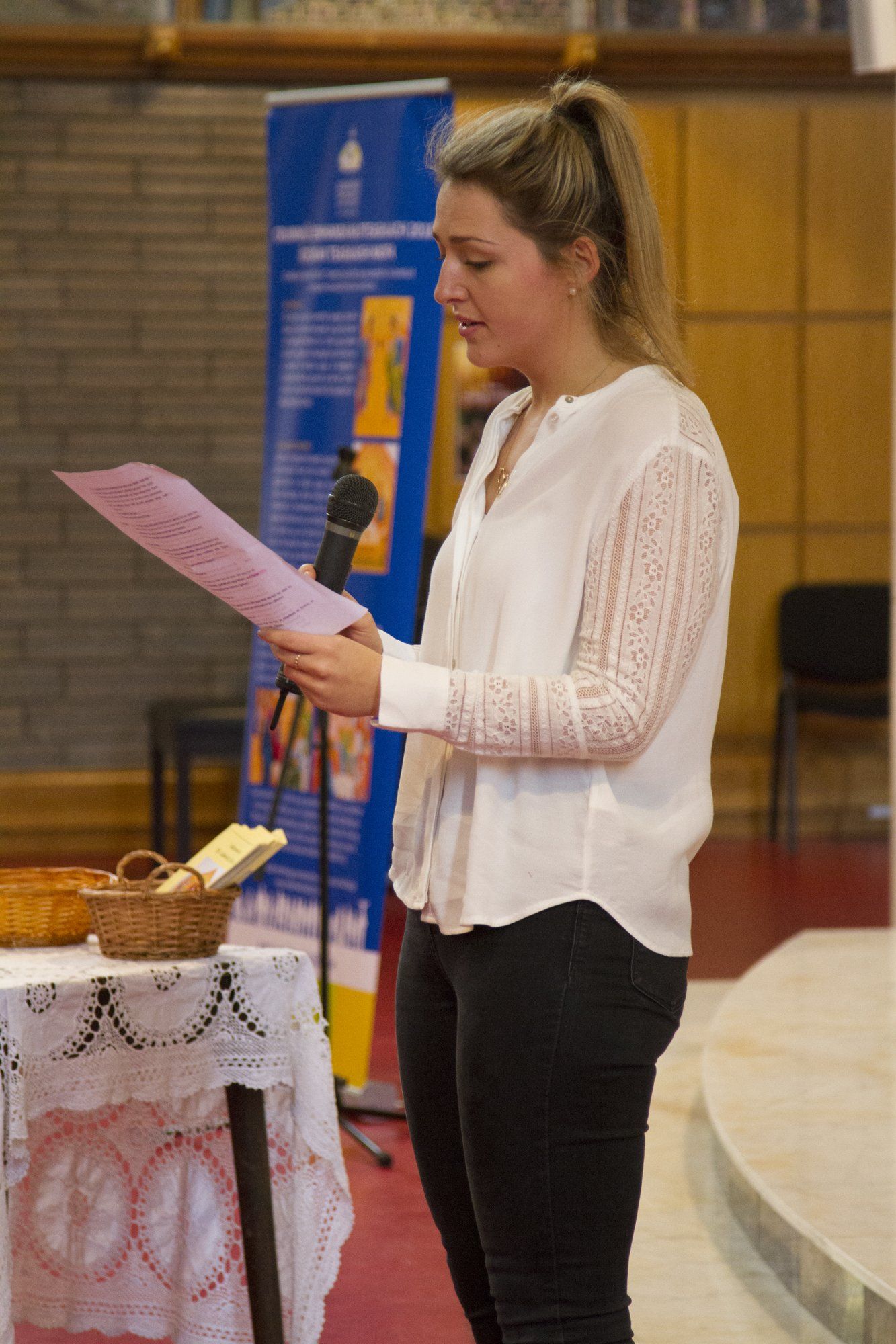 A woman is standing in front of a microphone reading a piece of paper.