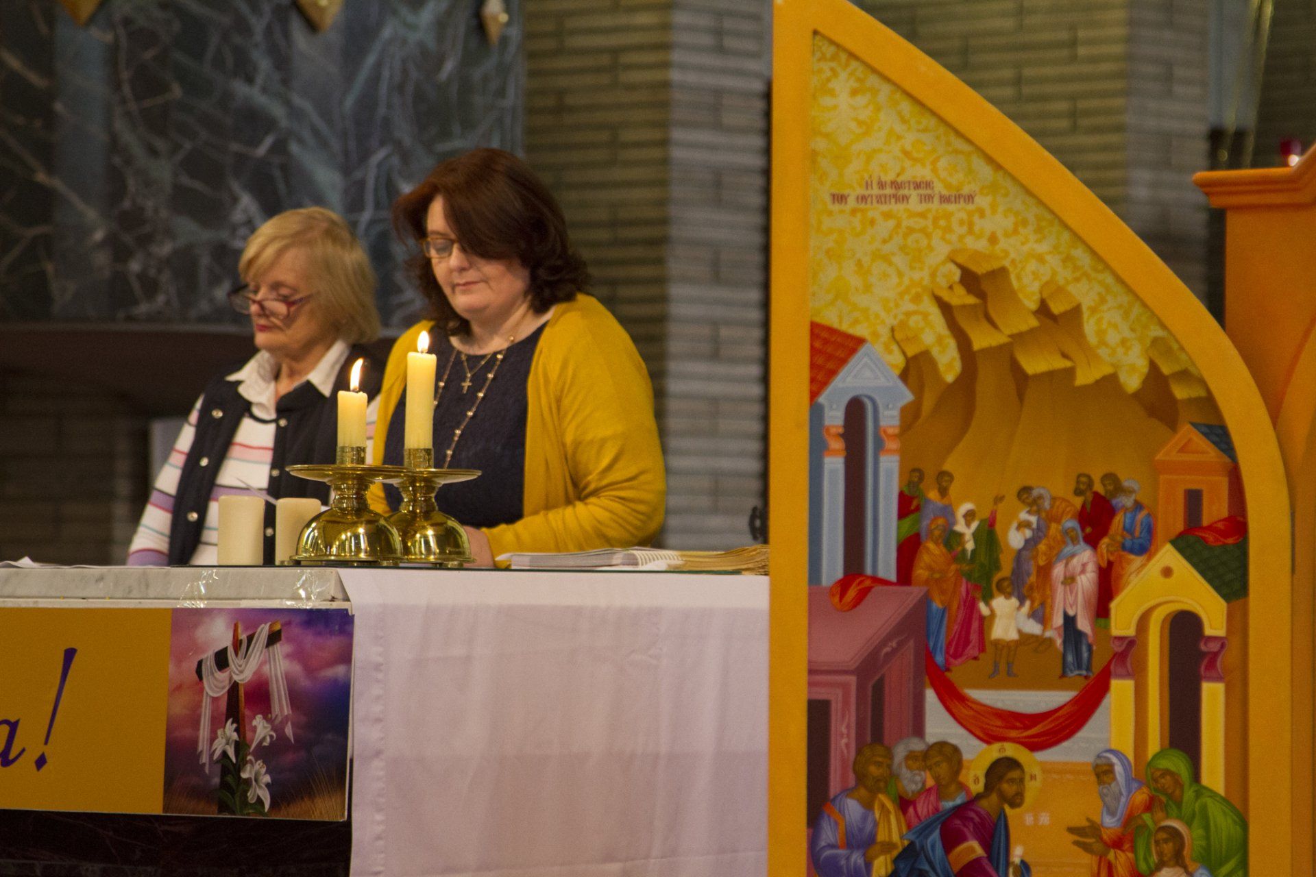 Two women are sitting at a table in a church with candles.