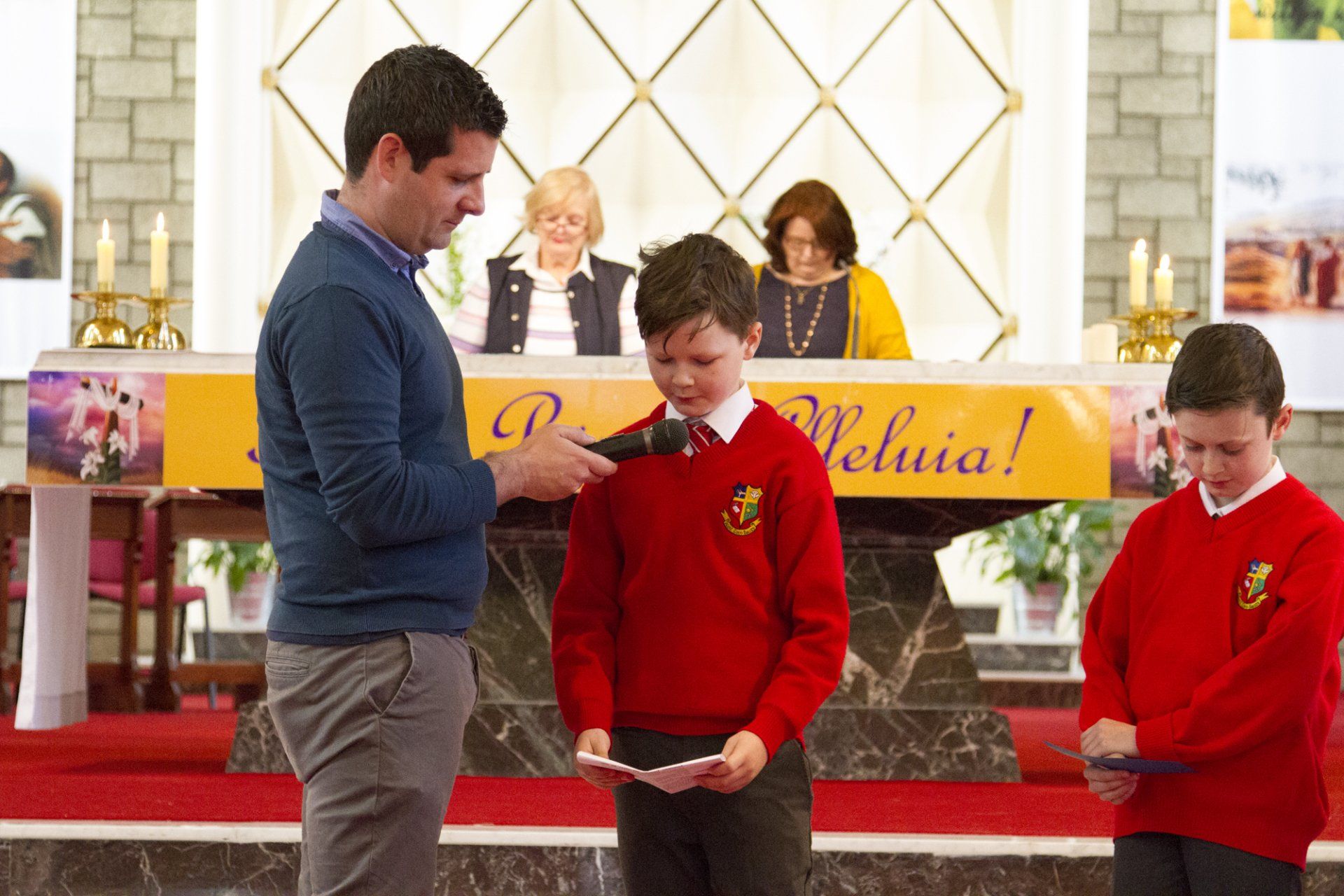 A man is talking to two young boys in red sweaters in a church