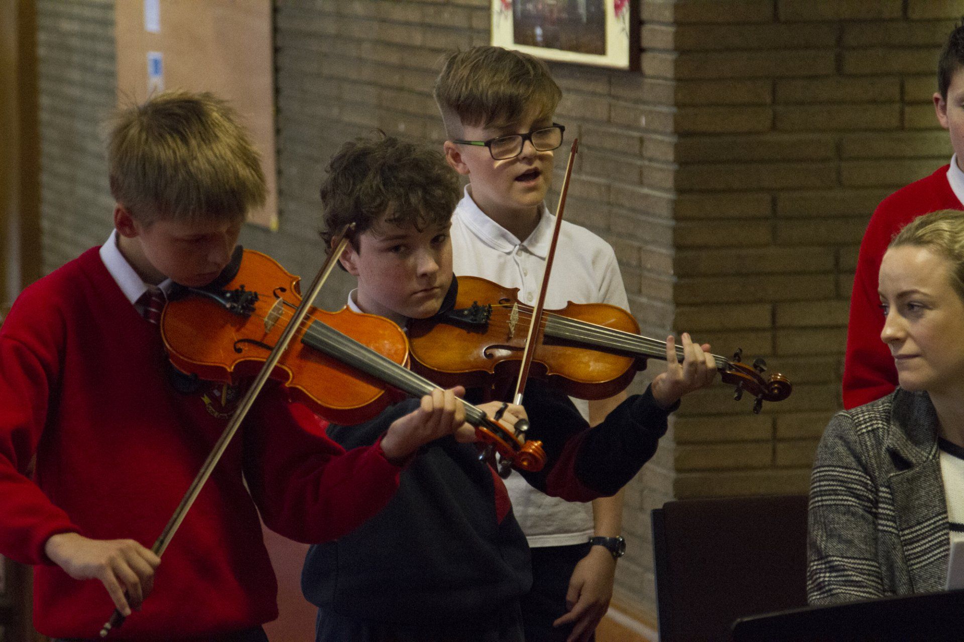 A group of young boys are playing violins in front of a woman.