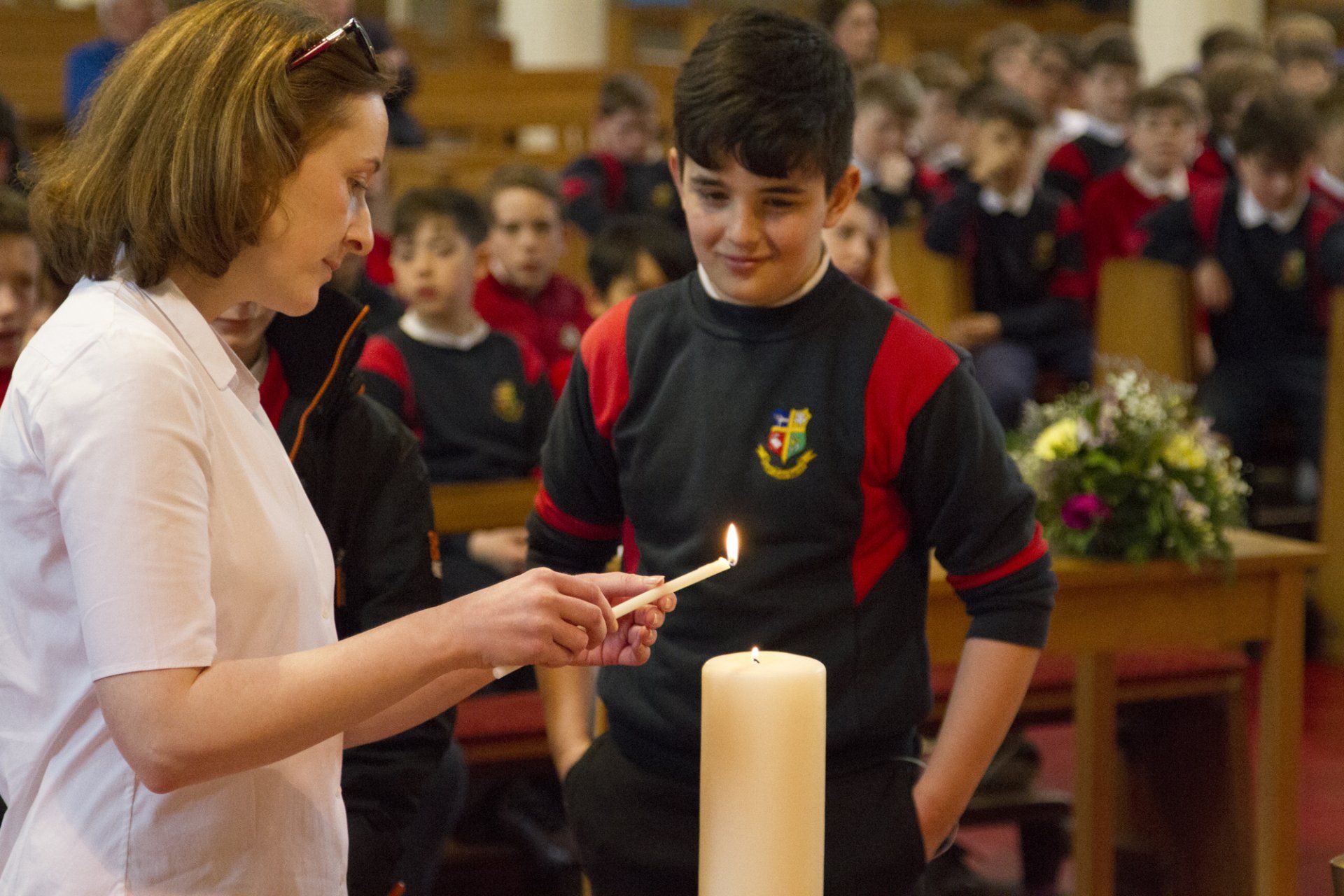 A woman is lighting a candle in front of a boy in a church.