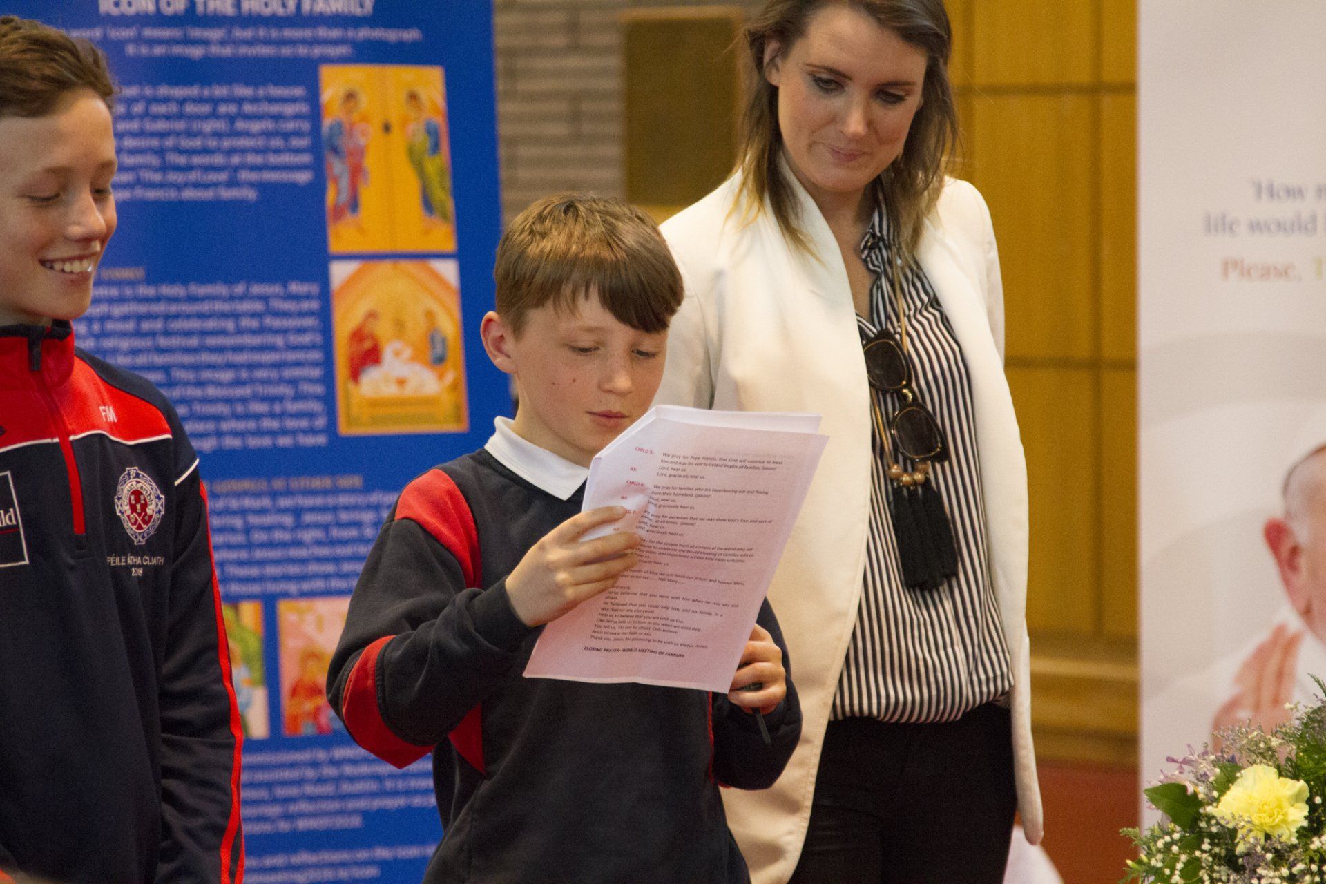 A boy is reading a piece of paper while a woman stands behind him.