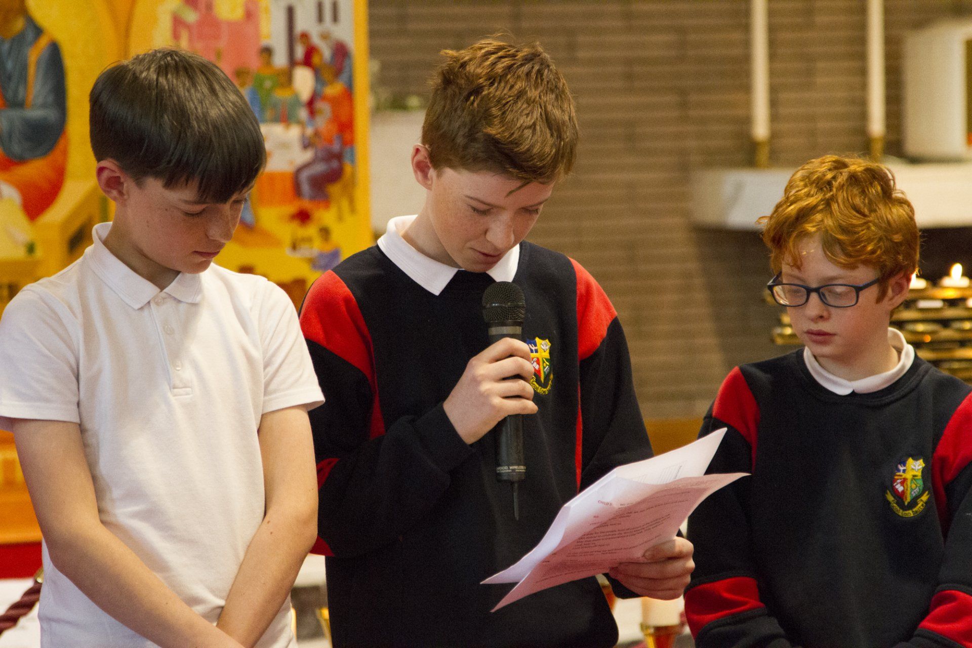 Three young boys are standing next to each other and one of them is holding a microphone.