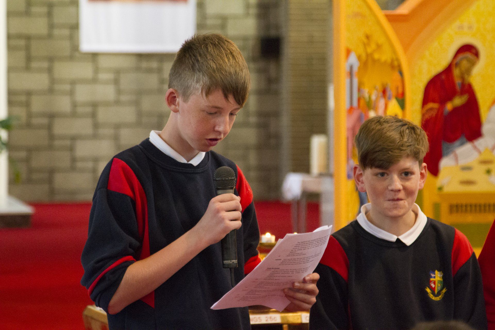 A boy is holding a microphone and reading a piece of paper in a church.
