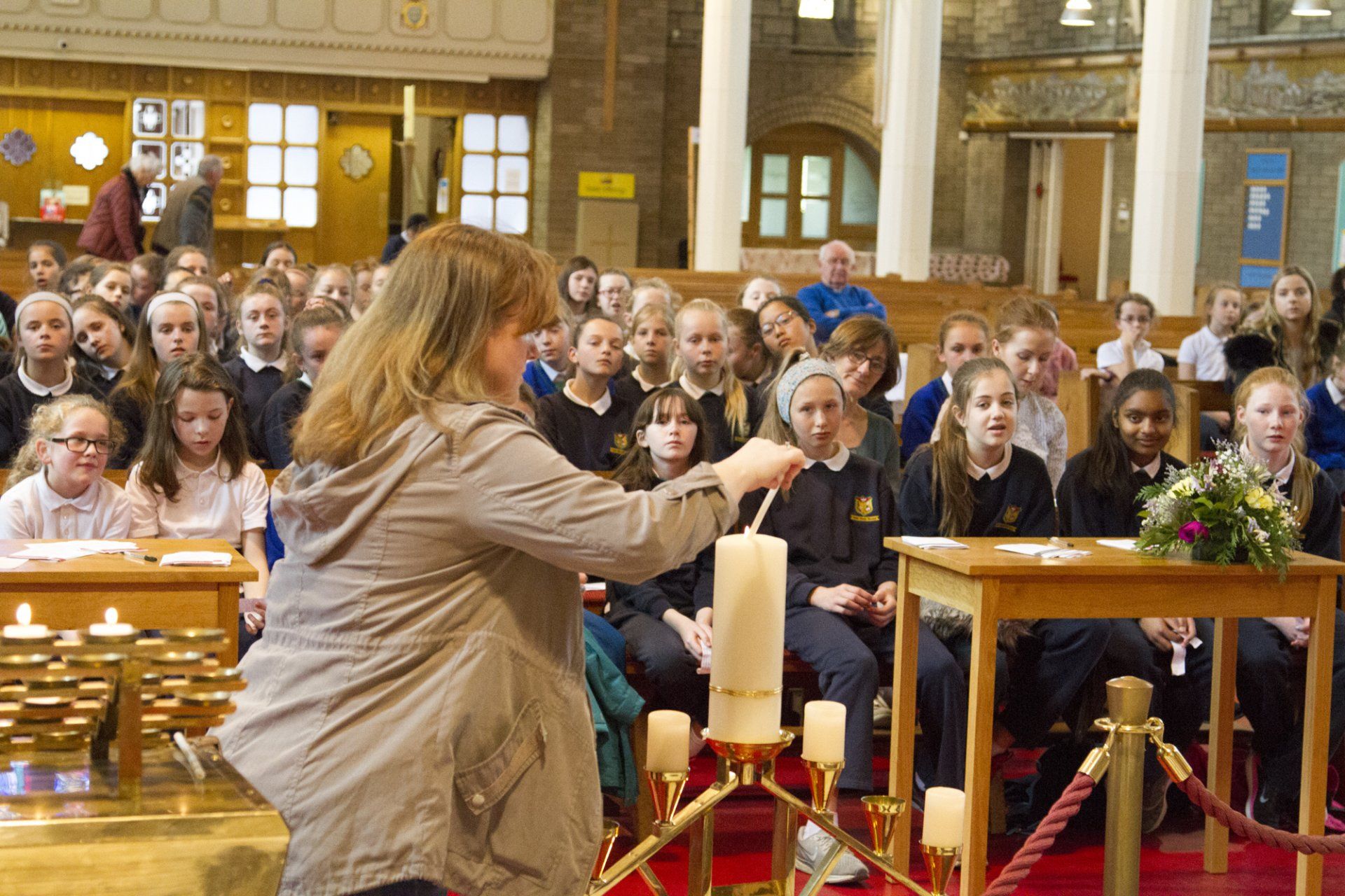 A woman is lighting a candle in front of a crowd of people in a church.