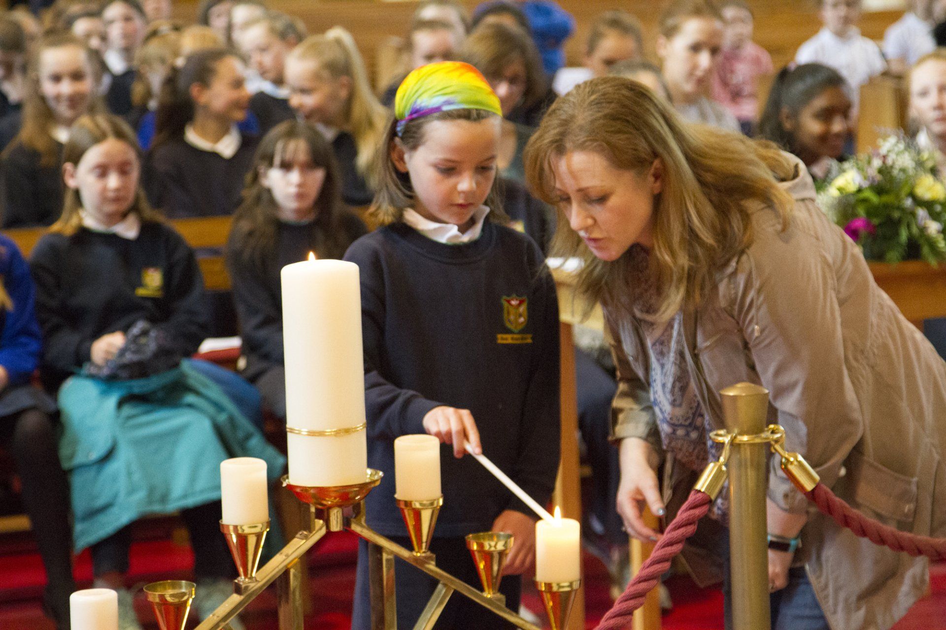 A woman is helping a young girl light a candle in a church.