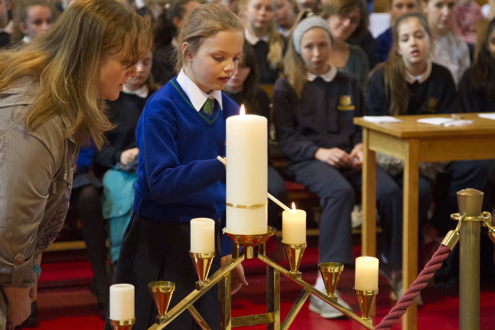 A girl is lighting a candle in a church while a woman looks on.