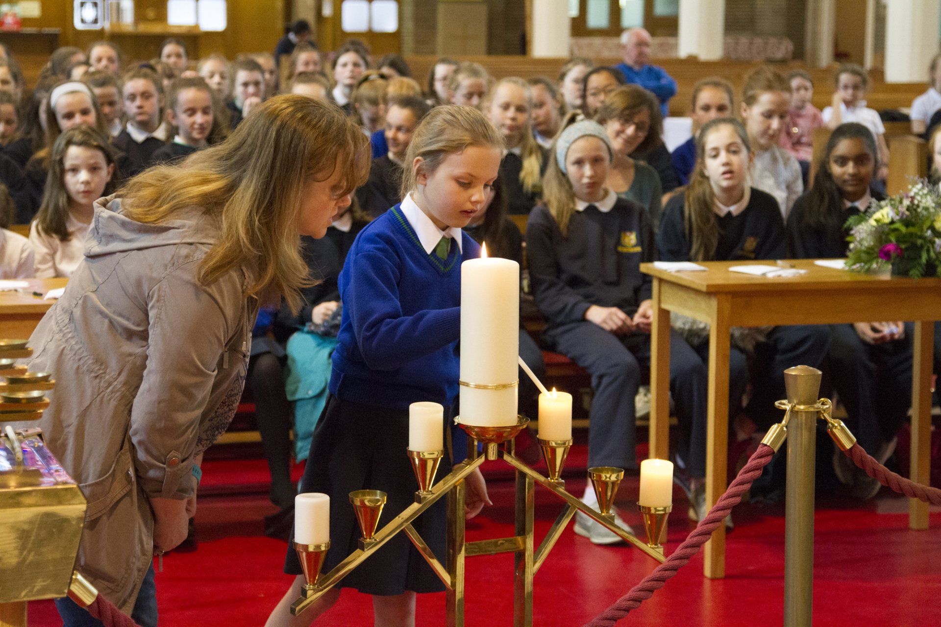 A girl is lighting a candle in front of a crowd of people in a church.